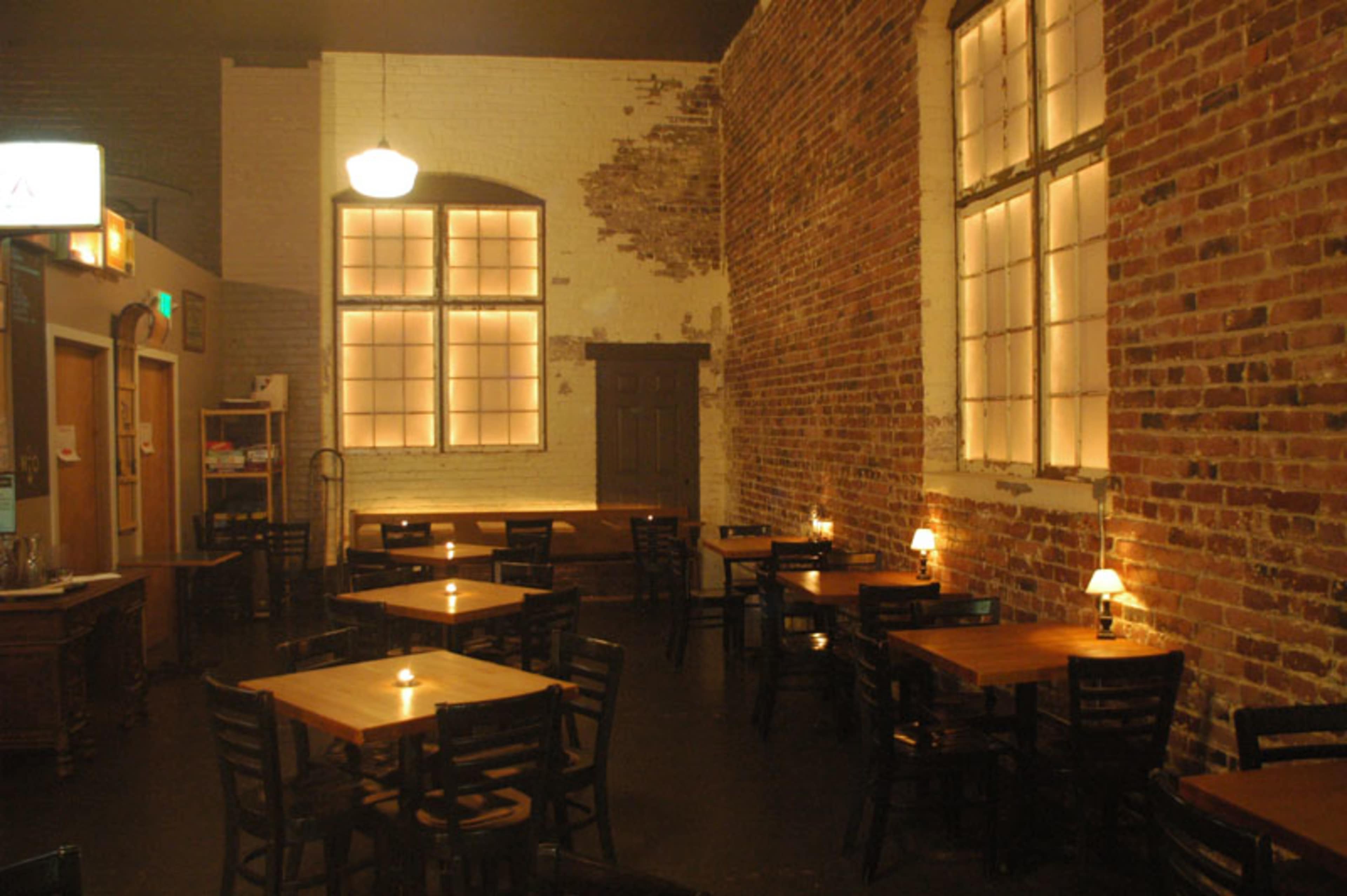 A rustic restaurant interior with brick walls, wooden tables, and soft lighting from candles.