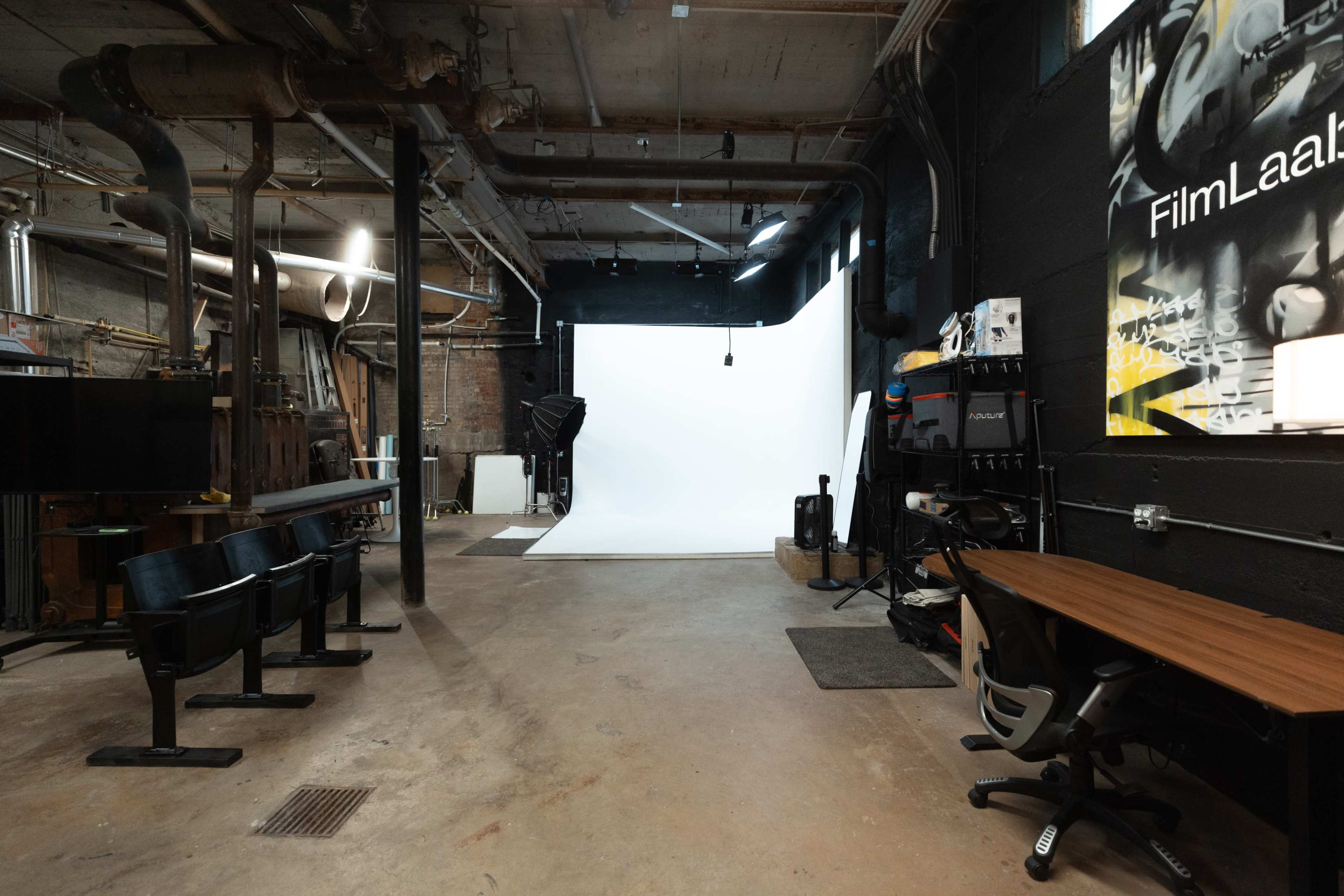 A studio space with a white backdrop, seating, a desk with an office chair, and various photography equipment.