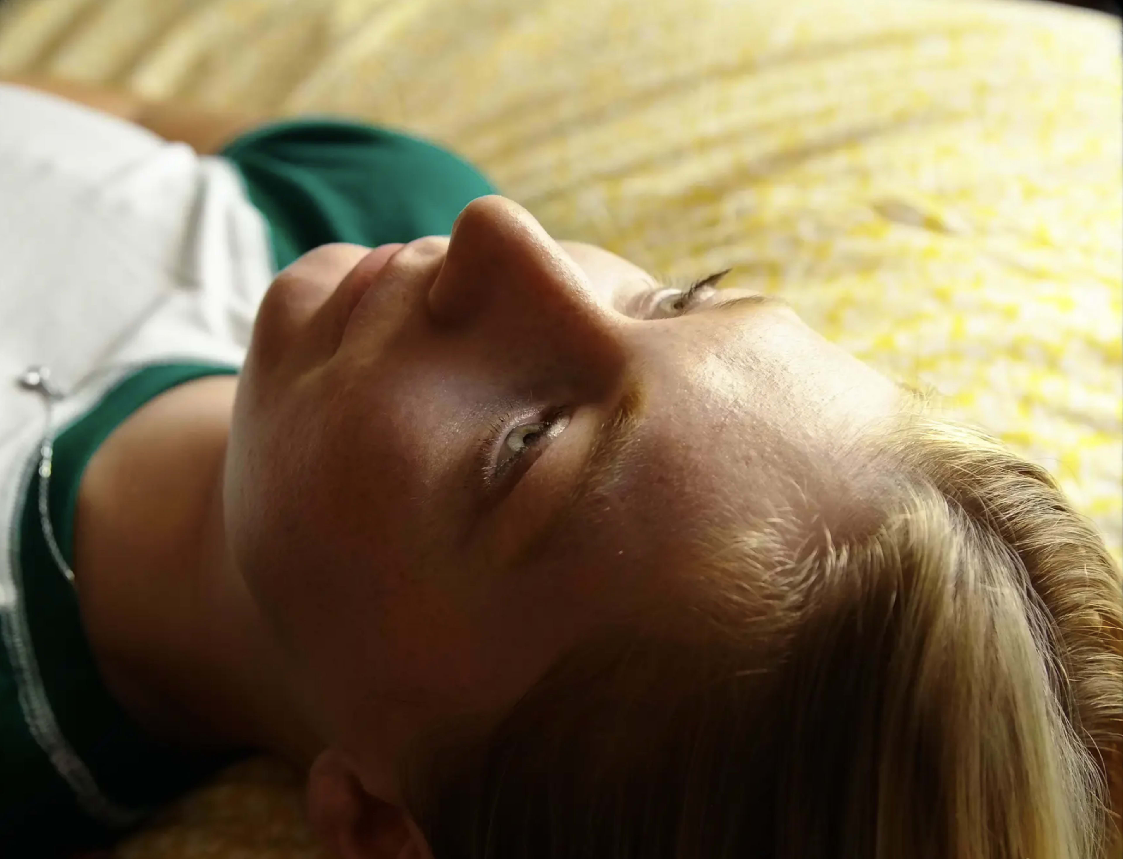 A person lies on a bed with a yellow patterned blanket, gazing upwards.