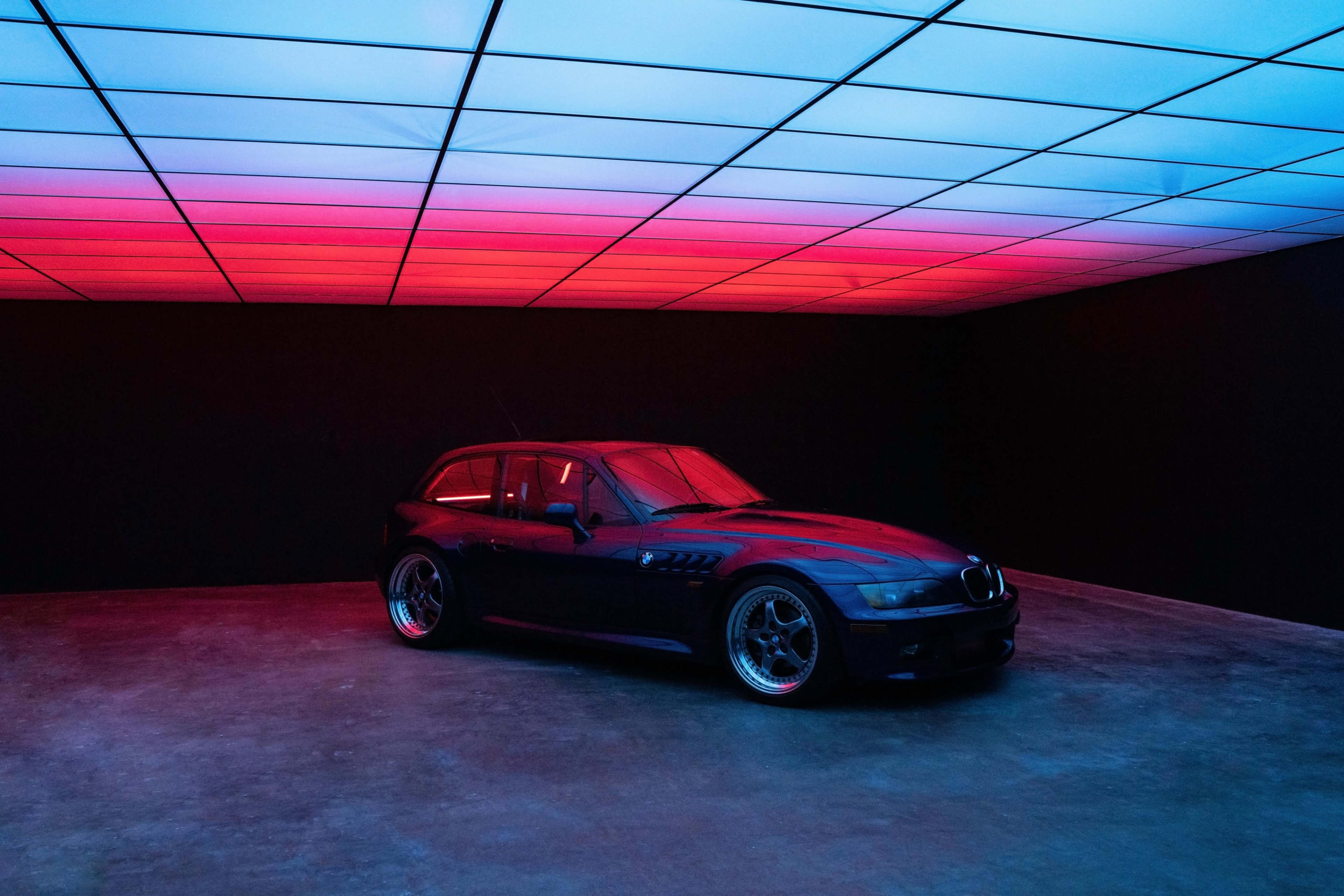 A BMW car with a sleek design is positioned in a dimly lit room featuring a colorful, illuminated ceiling.