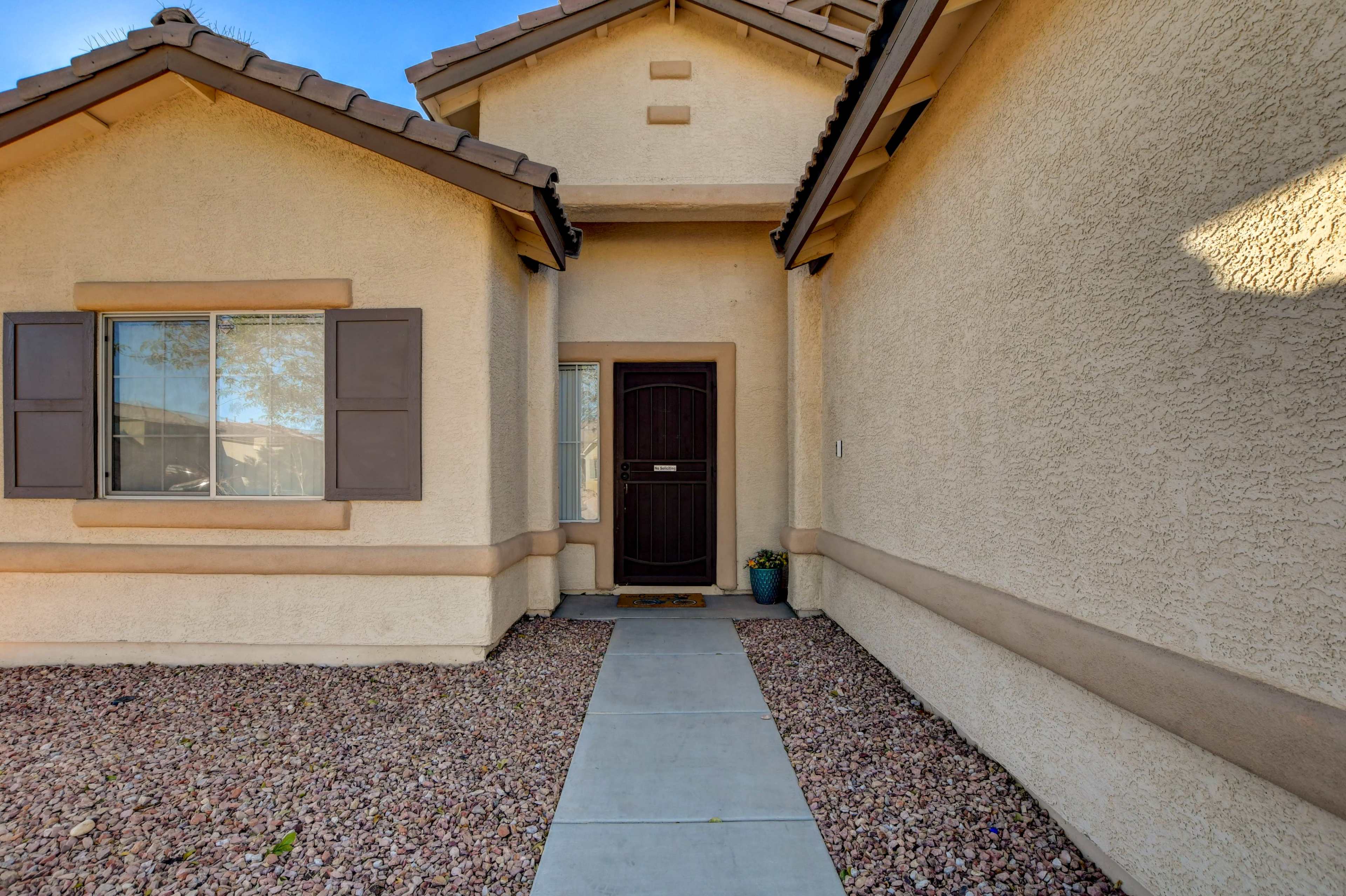 The entrance of a house with a front door, flanked by two windows and a walkway leading to the door.