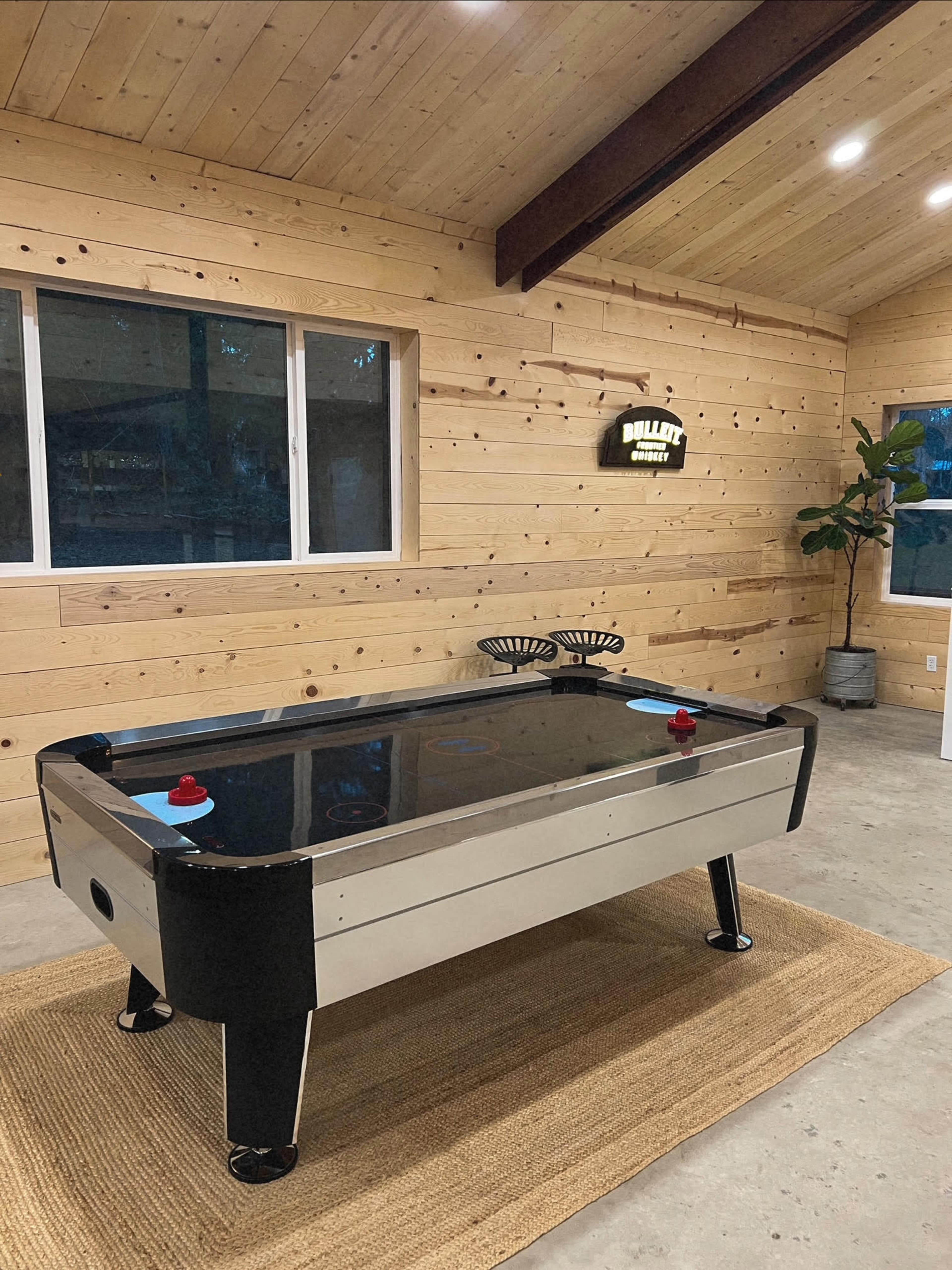 An air hockey table placed in a room with wooden walls and a plant in the corner.