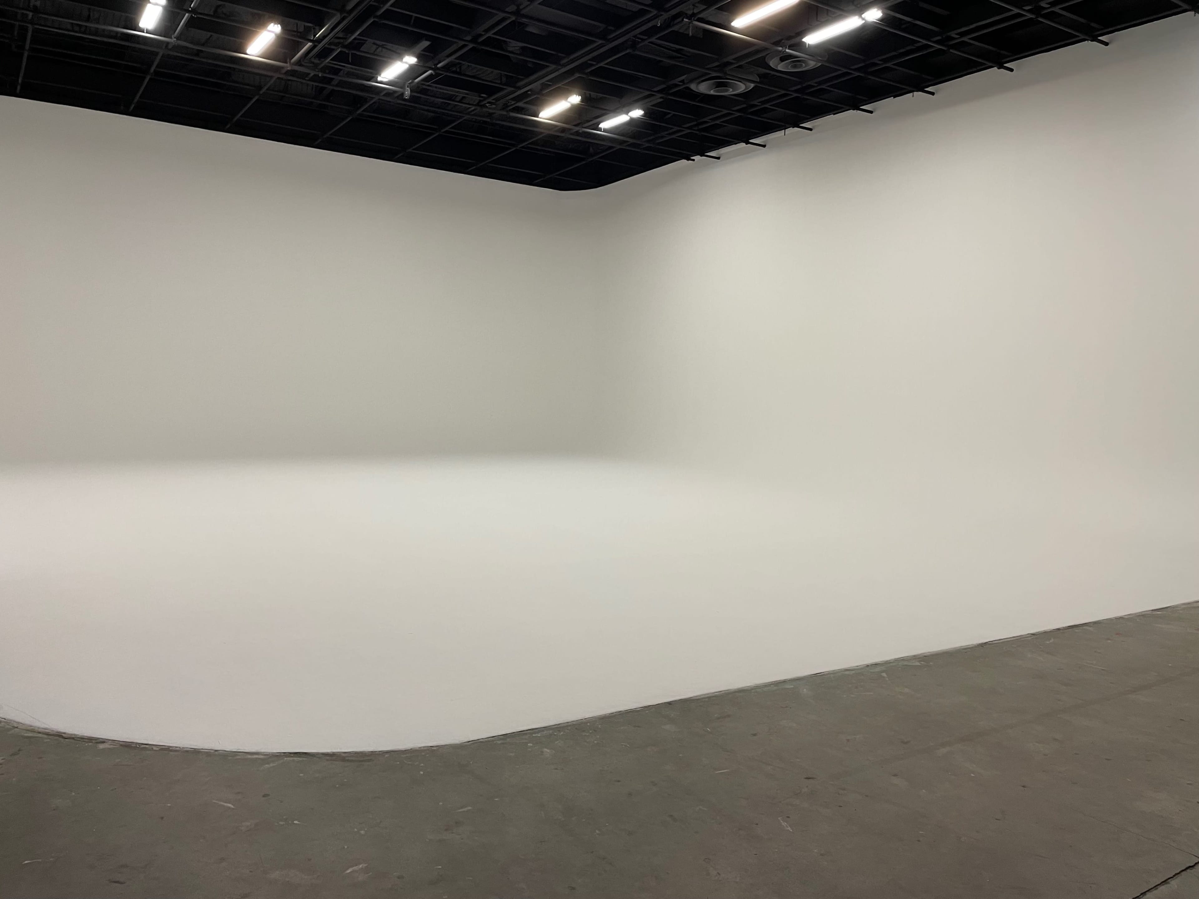 The image shows a spacious, empty studio with white walls and a seamless floor.