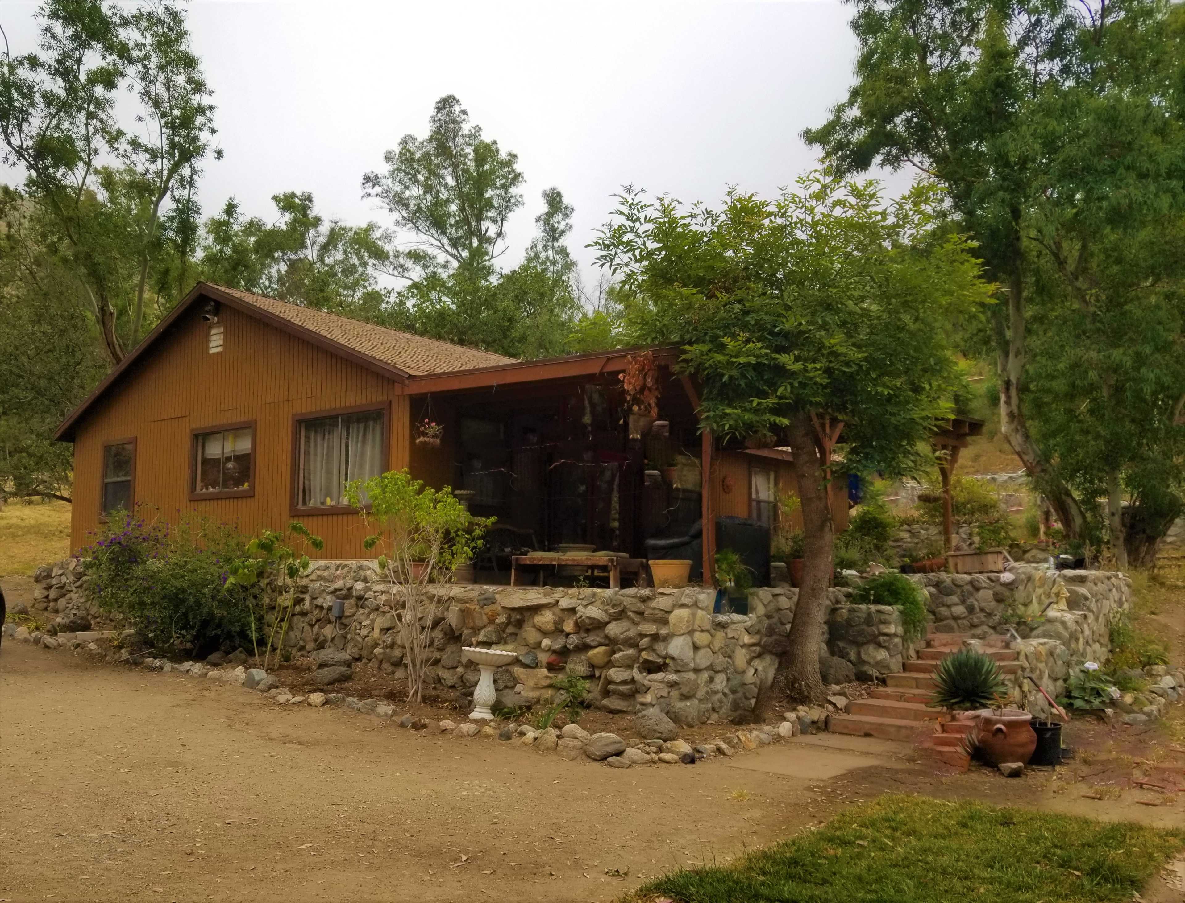 A wooden house with a stone foundation is surrounded by trees and a landscaped yard.