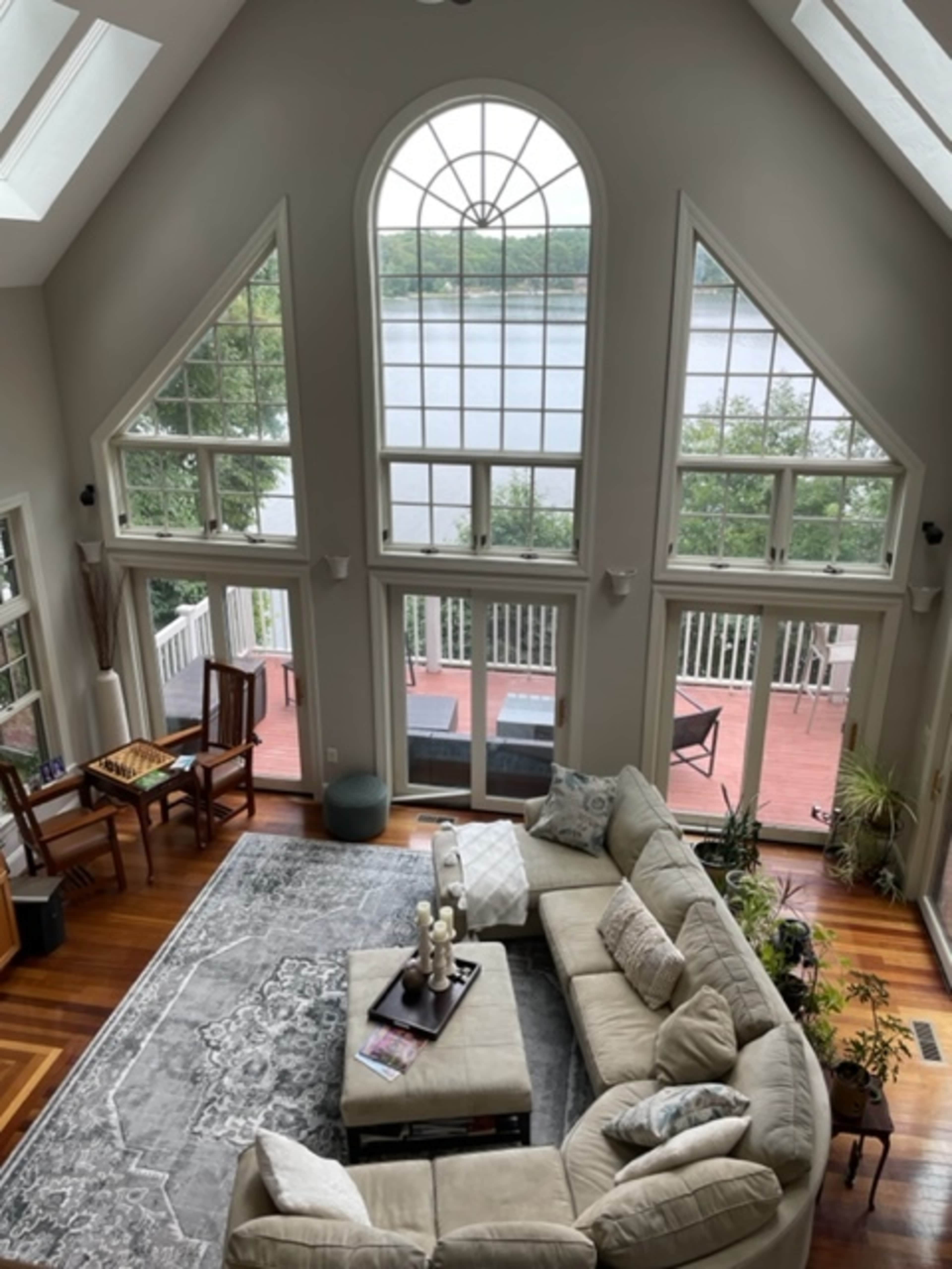 A spacious living room features large windows with a view of a lake, a sectional sofa, and a dining table by the window.