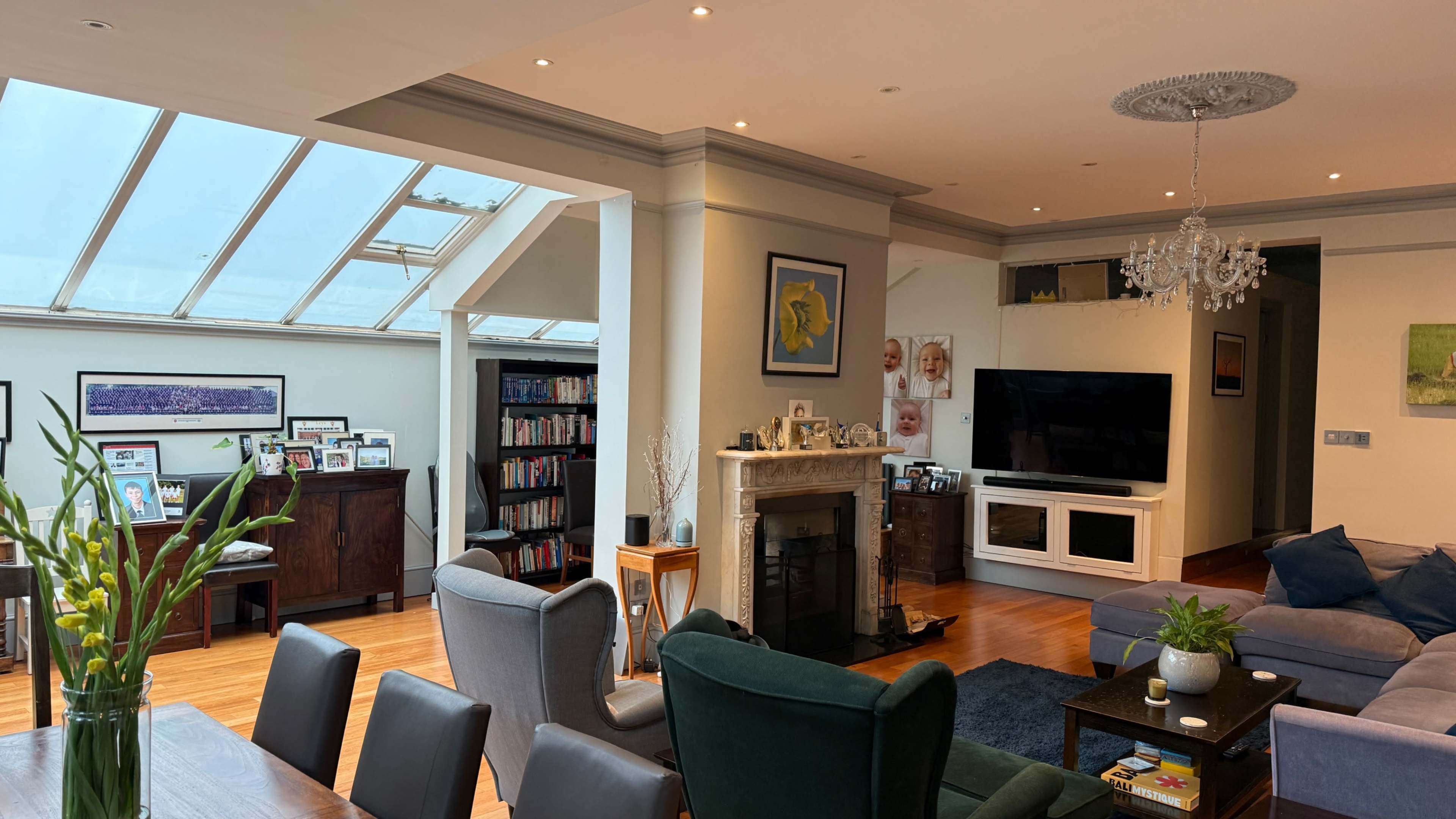 The image shows a spacious living room with a glass ceiling, modern furniture, a television, and bookcases along the walls.