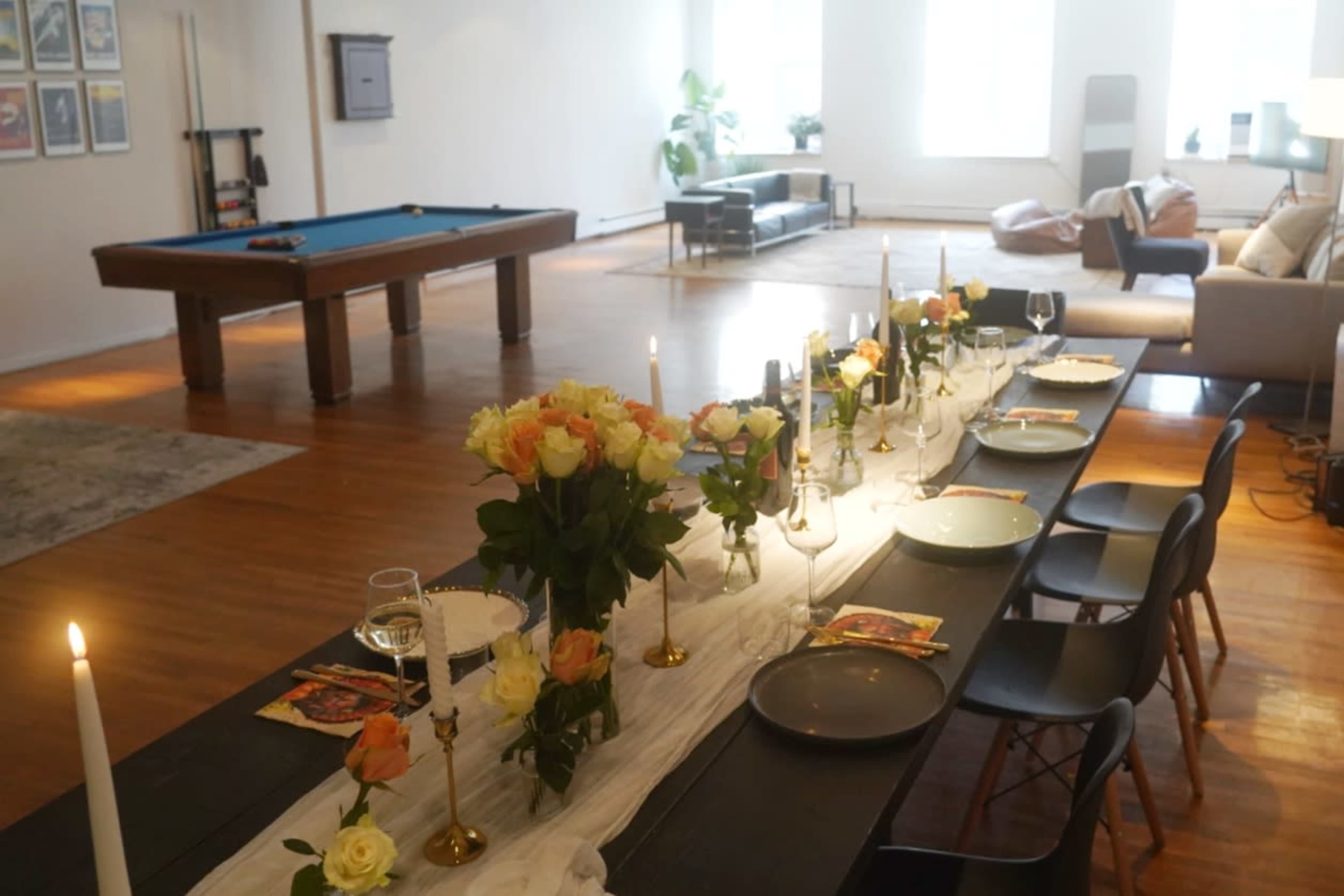 A long dining table adorned with flowers and candles is set for a meal in a spacious room featuring a pool table and comfortable seating.