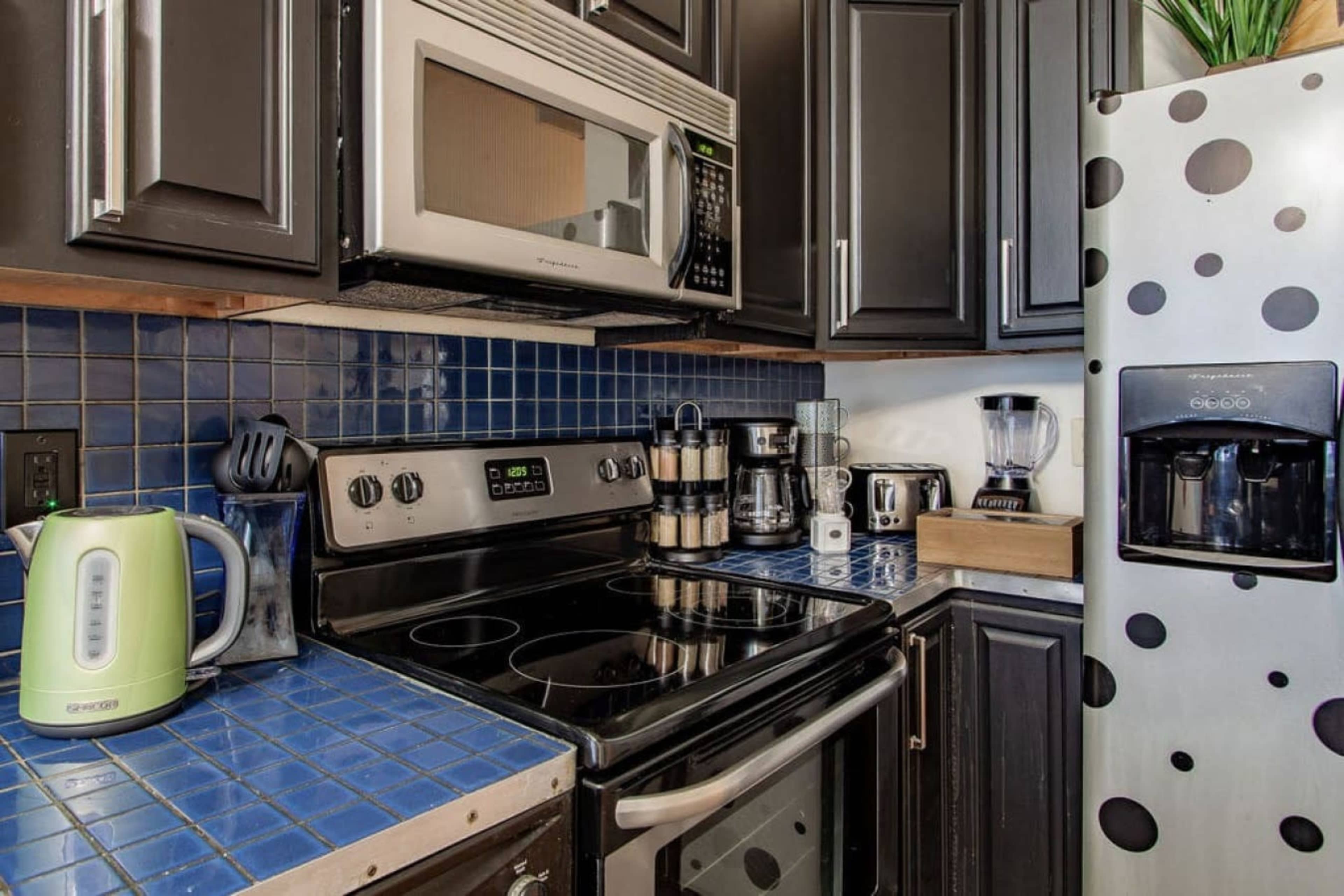 The kitchen features dark cabinets, a stainless steel refrigerator with a water dispenser, and a blue tiled countertop with various appliances.