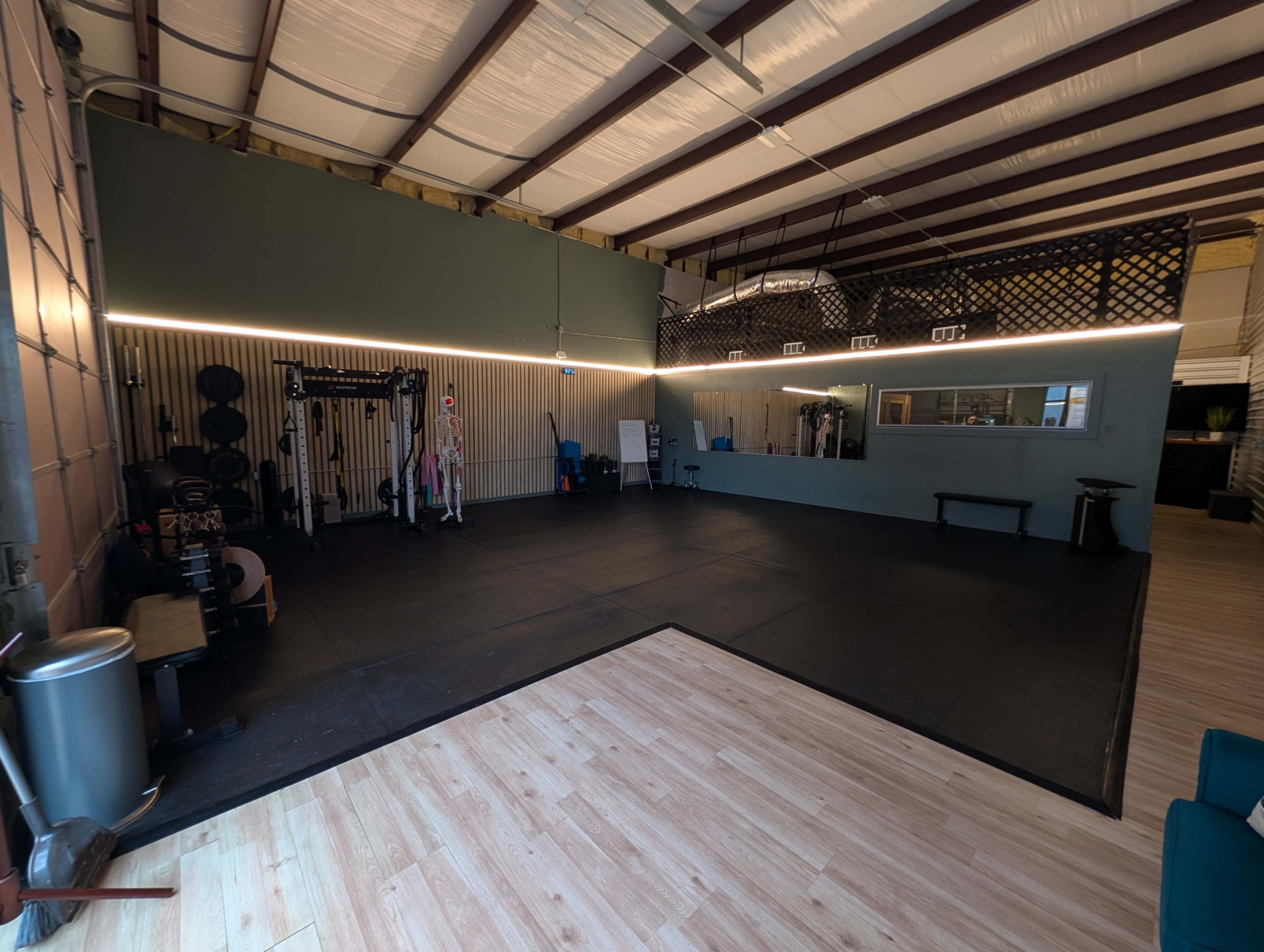 The image shows a spacious gym interior with weightlifting equipment, a rubber floor, and natural lighting from windows.