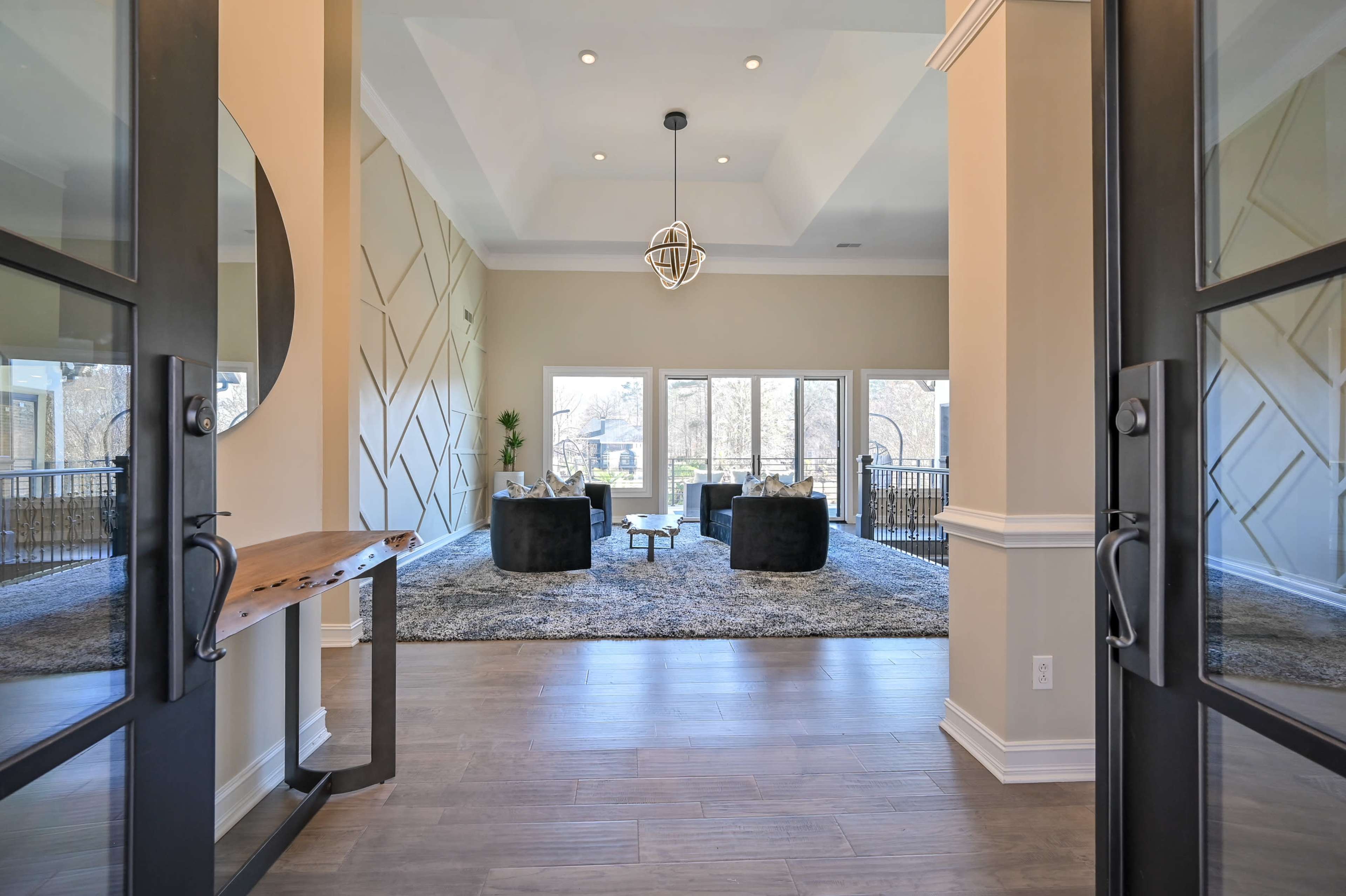 An entrance area leading into a spacious living room with large windows, modern furniture, and a plush rug.