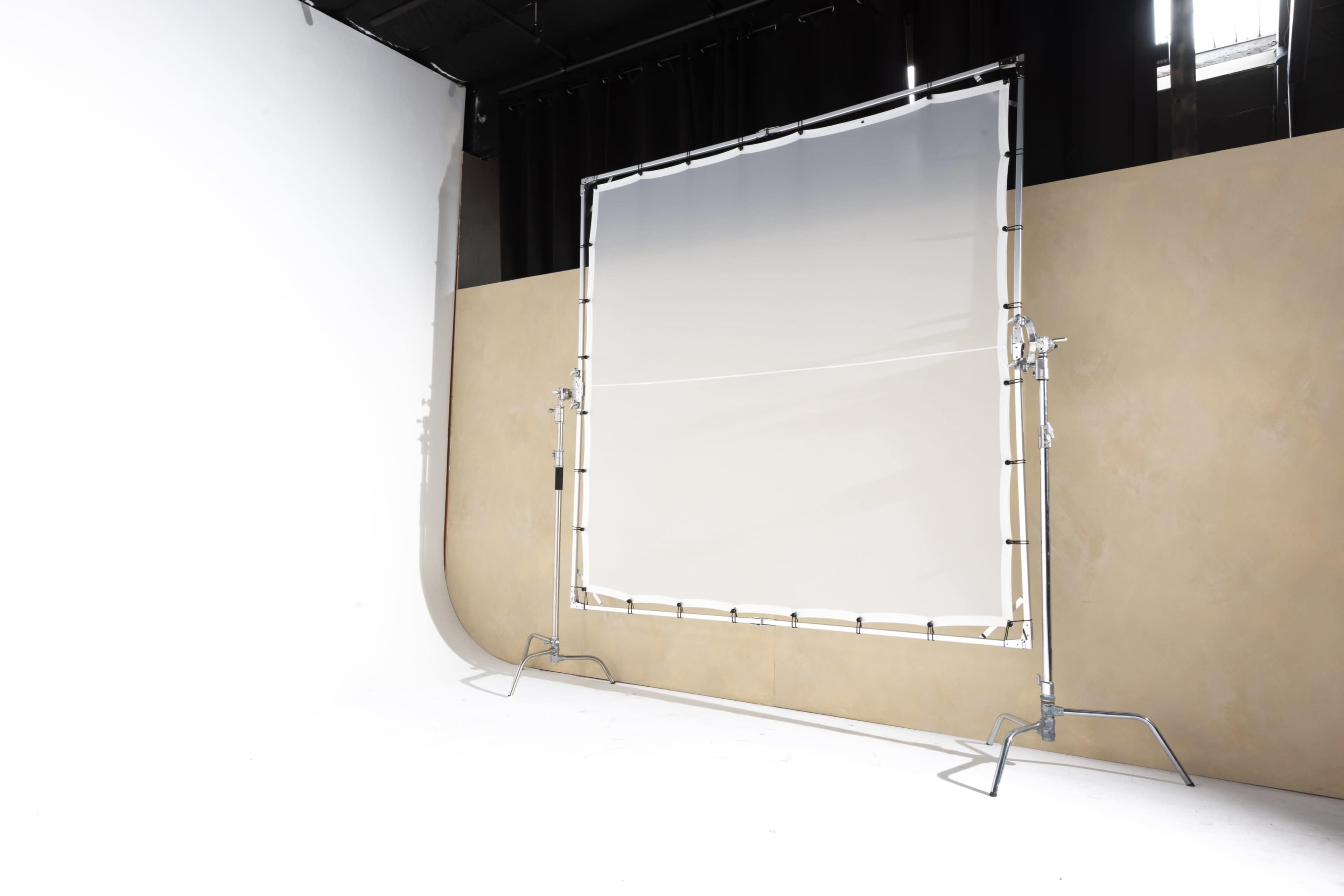 A photography studio features a large white backdrop framed on a stand against a tan wall.