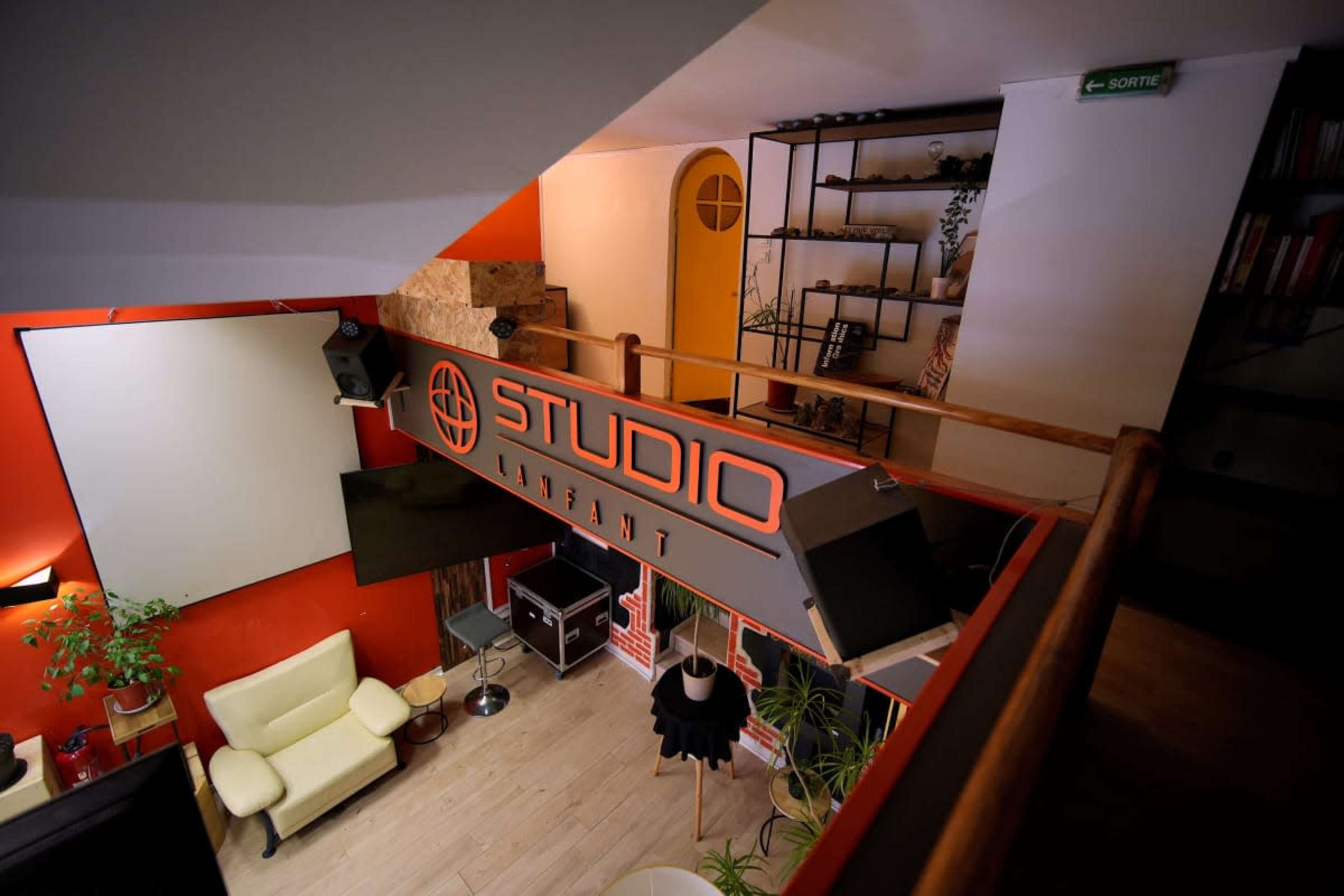 The image shows an interior view of a studio with a prominent "STUDIO" sign, featuring modern decor, a seating area, and shelves with plants.