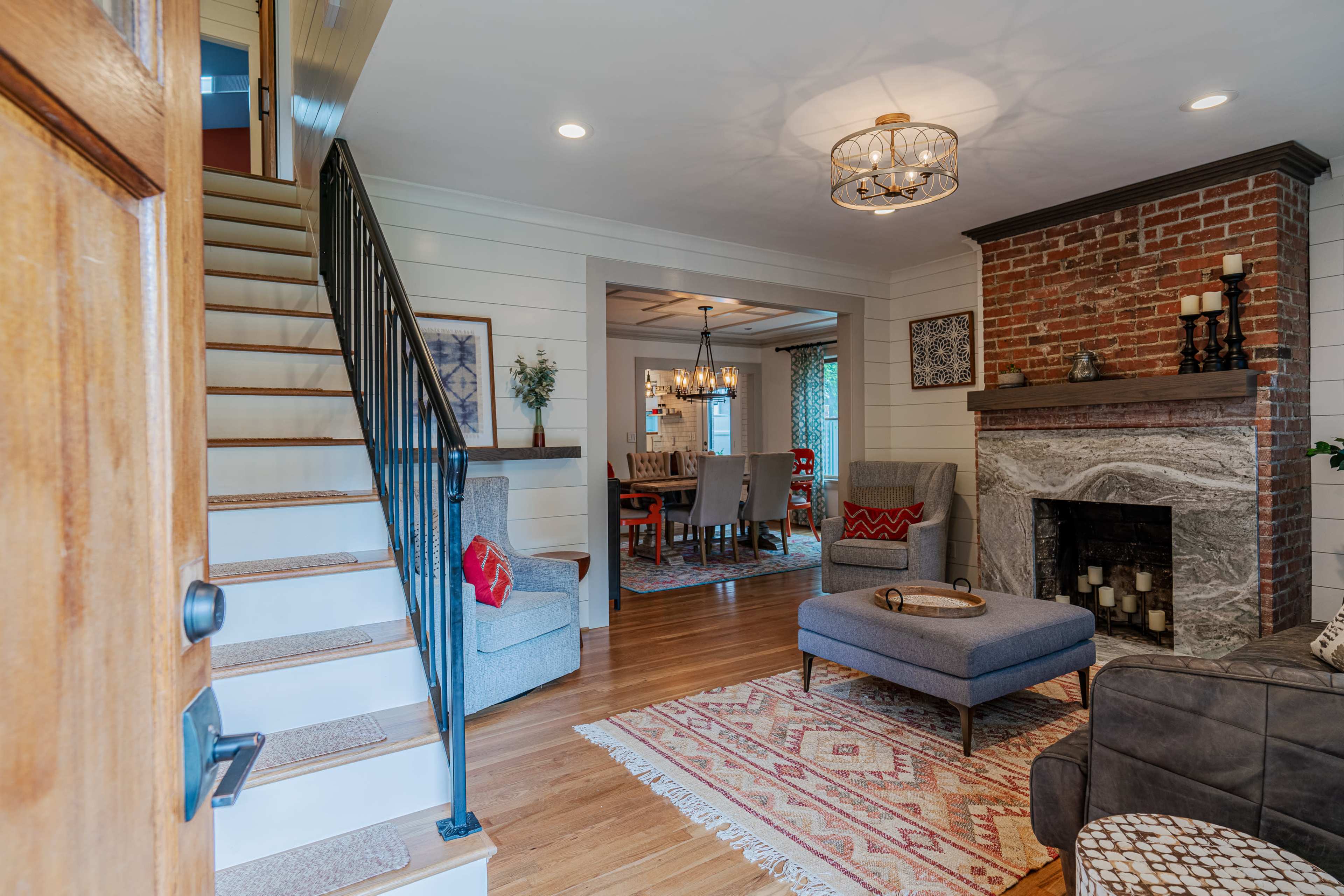 A cozy living room features a brick fireplace, a staircase leading to an upper level, and a dining area visible in the background.