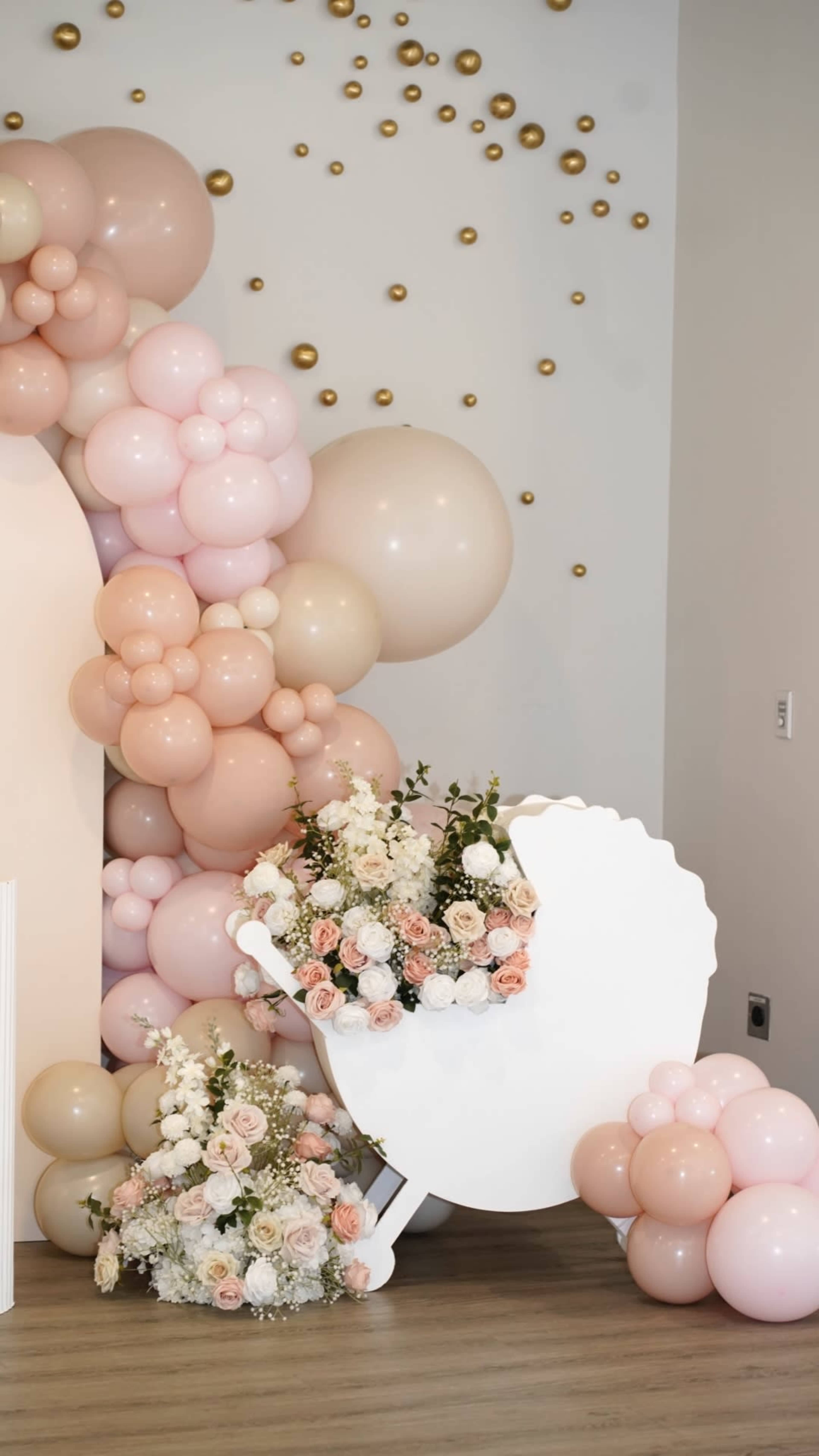 A decorative scene features a large arrangement of pink and beige balloons alongside floral arrangements in a white shell-shaped display.