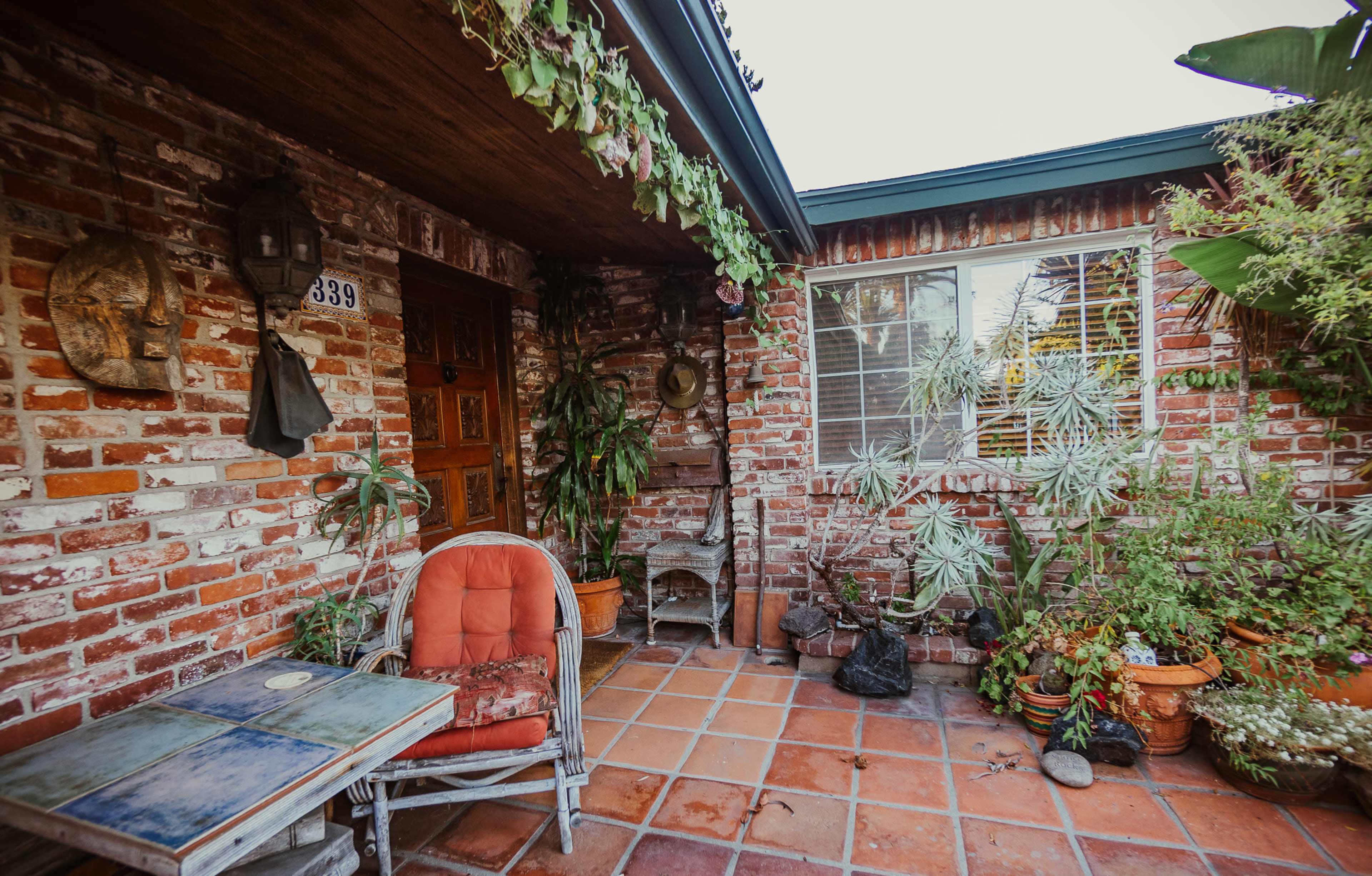 A brick exterior of a house with a small porch featuring potted plants and a rustic wooden door.