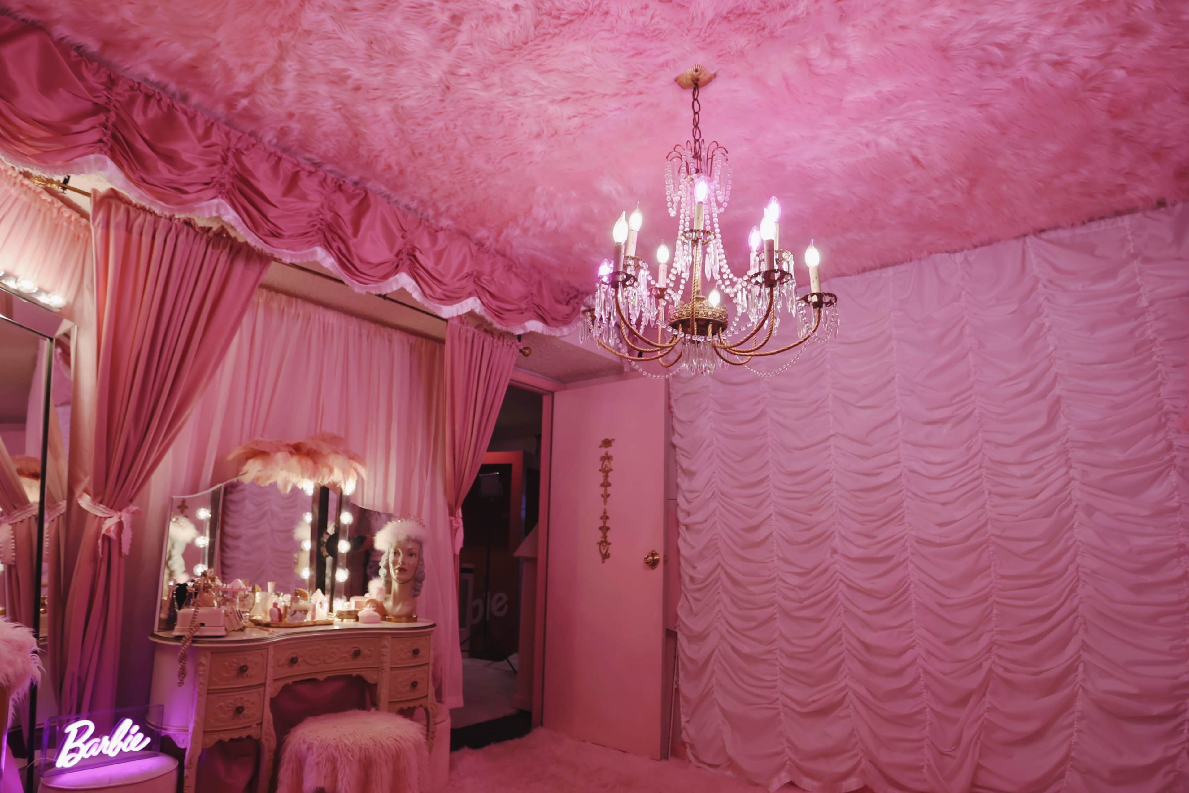 The room features pink walls and drapery, a chandelier, and a vanity set with a mirror.