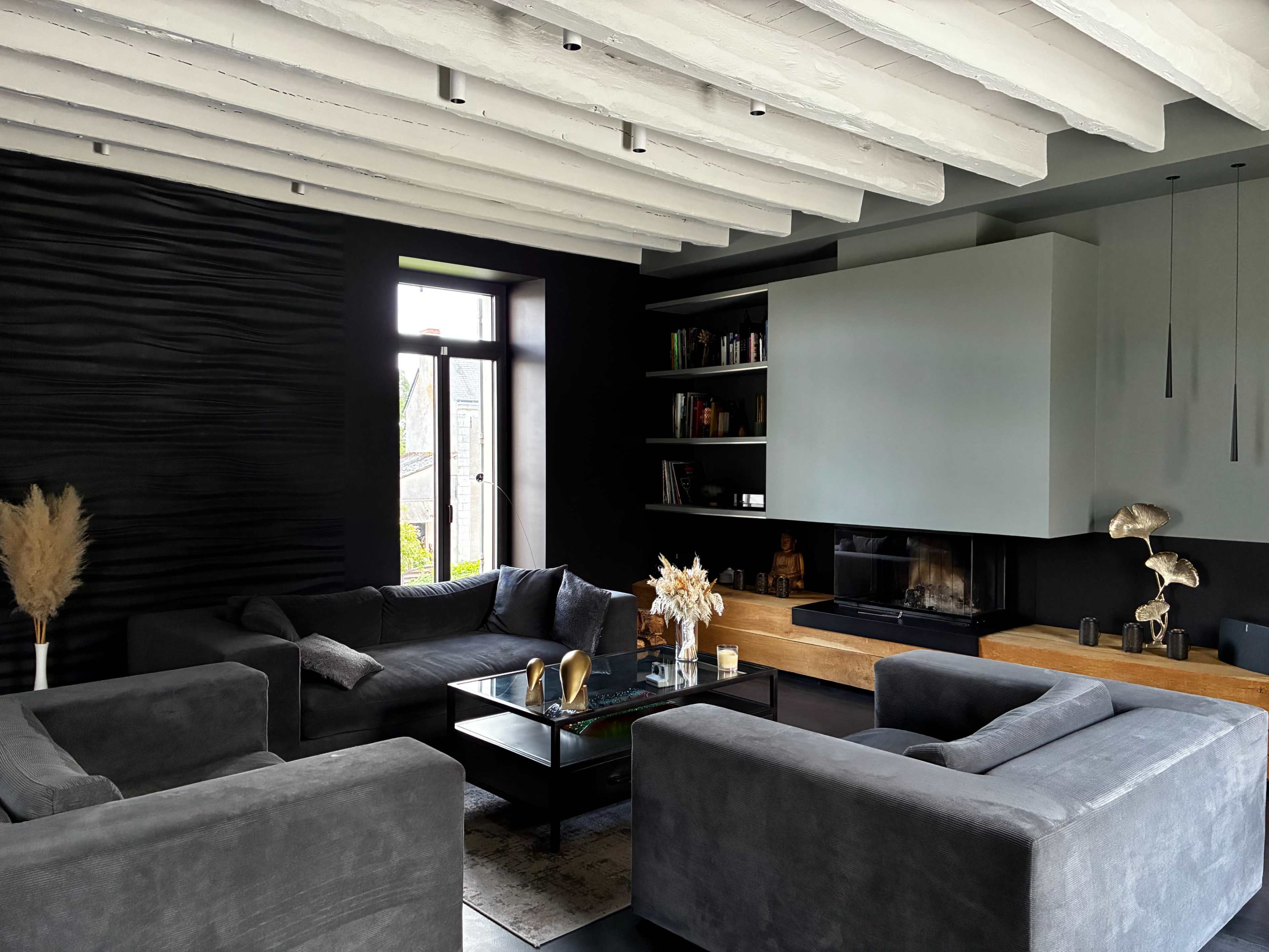 The image shows a modern living room with dark walls, a fireplace, and contemporary furniture arranged around a central coffee table.
