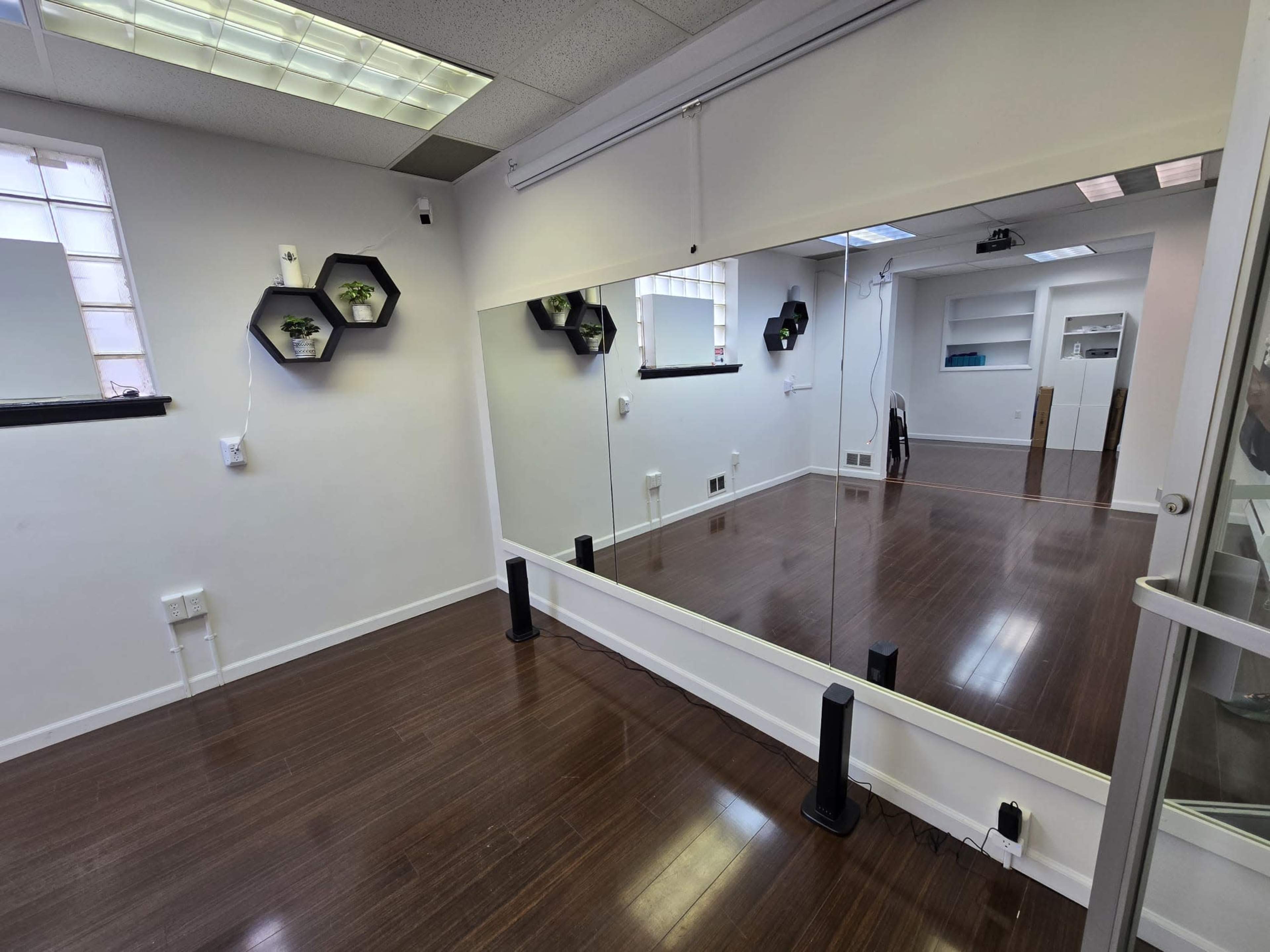 A mirrored wall in a room with hardwood flooring, featuring hexagonal wall shelves and minimal decor.