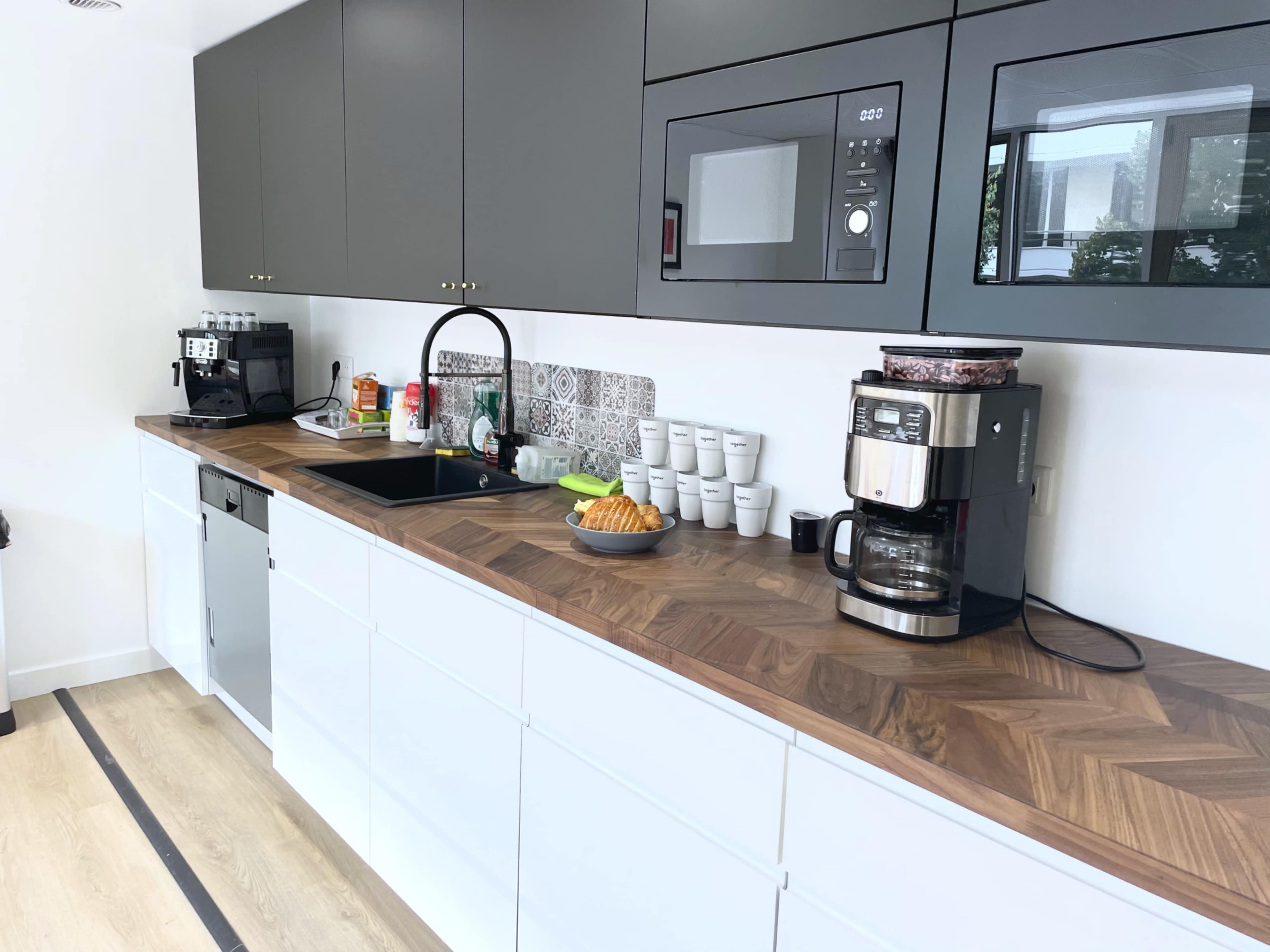 A modern kitchen with gray cabinets, a wooden countertop, a coffee maker, a microwave, and a sink, alongside various kitchen appliances and utensils.