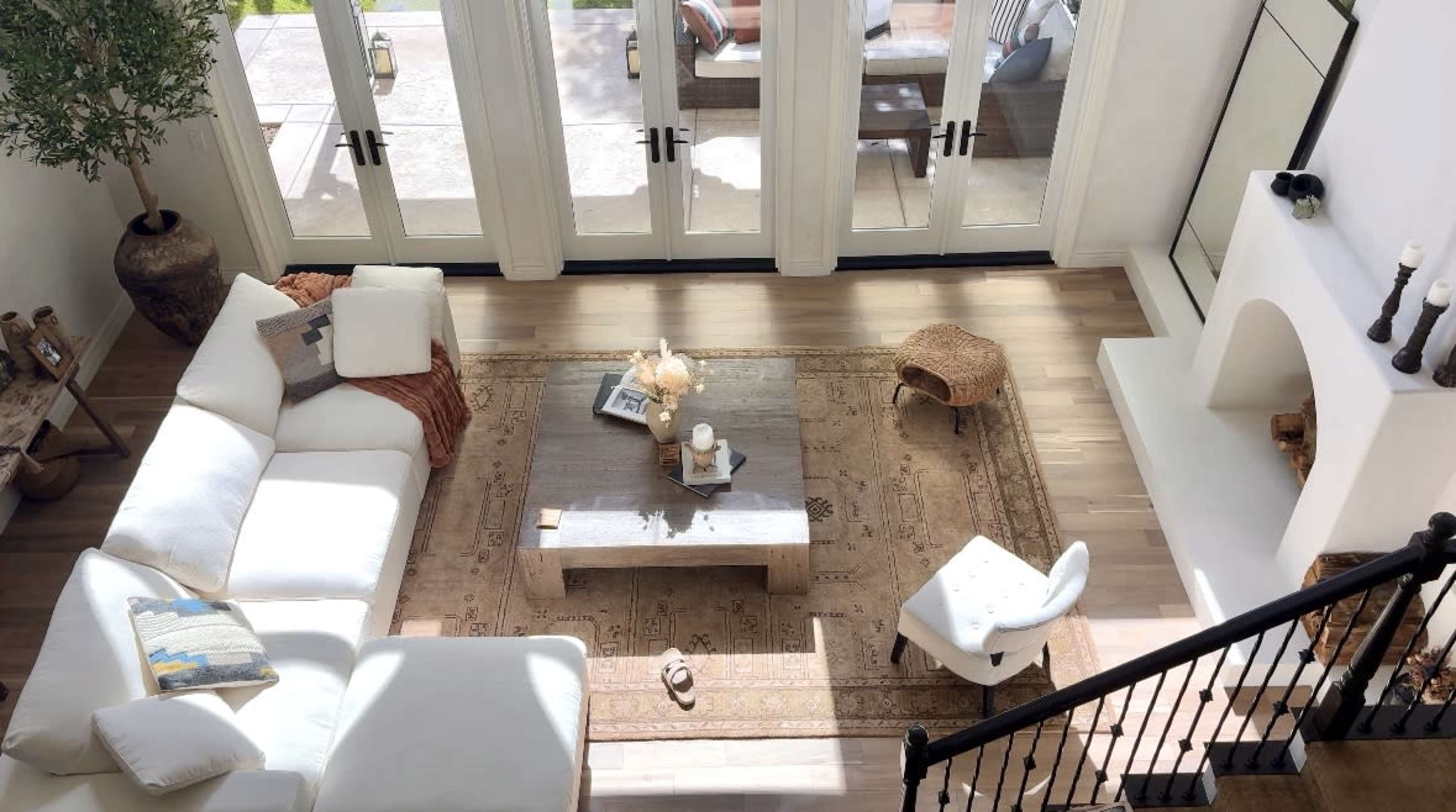 A spacious living room features a white sectional sofa, a wooden coffee table on a patterned rug, and large windows that open to an outdoor seating area.