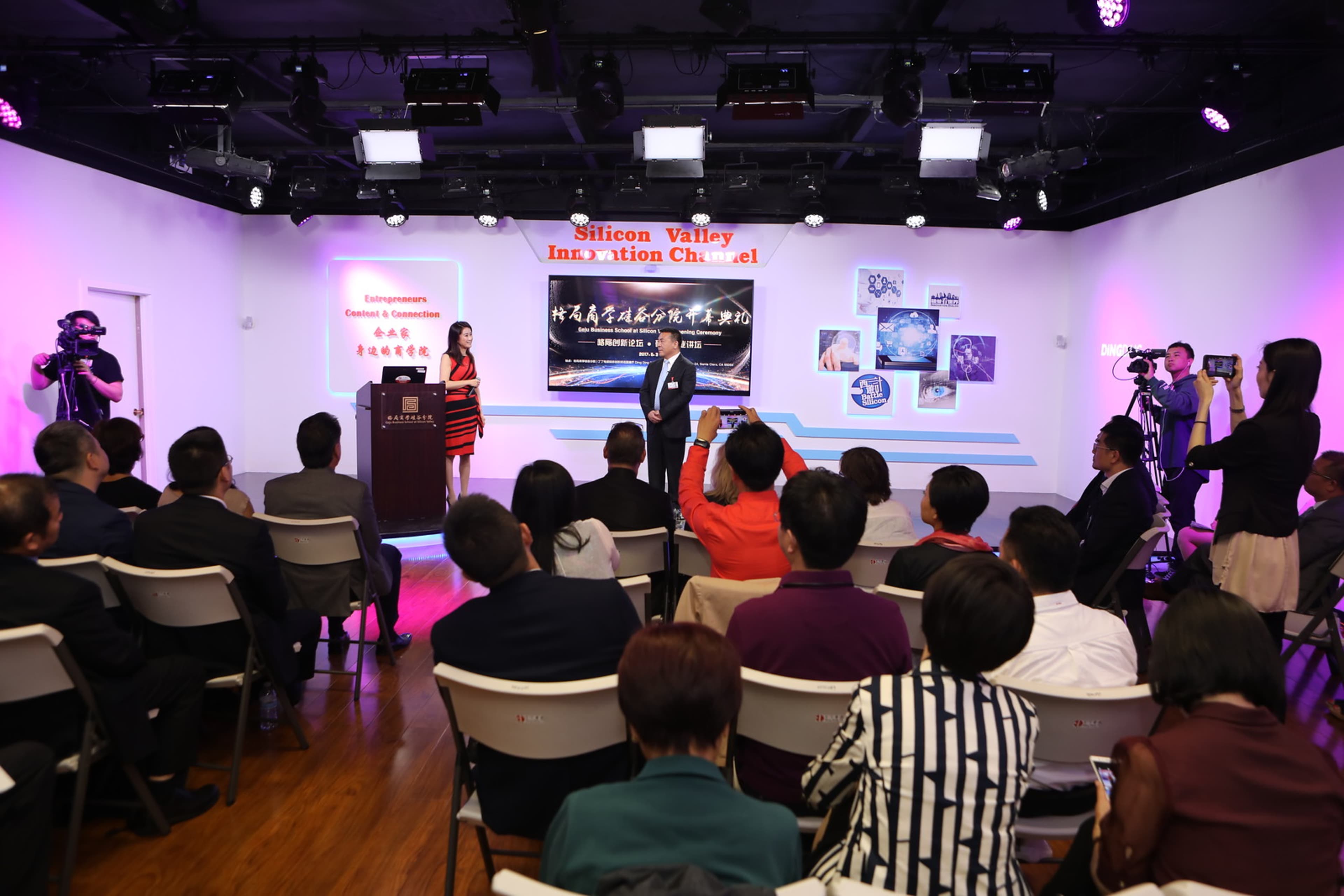 A speaker presents on stage at an event, while an audience watches in a well-lit room featuring multiple cameras and a backdrop displaying "Silicon Valley Innovation Channel."