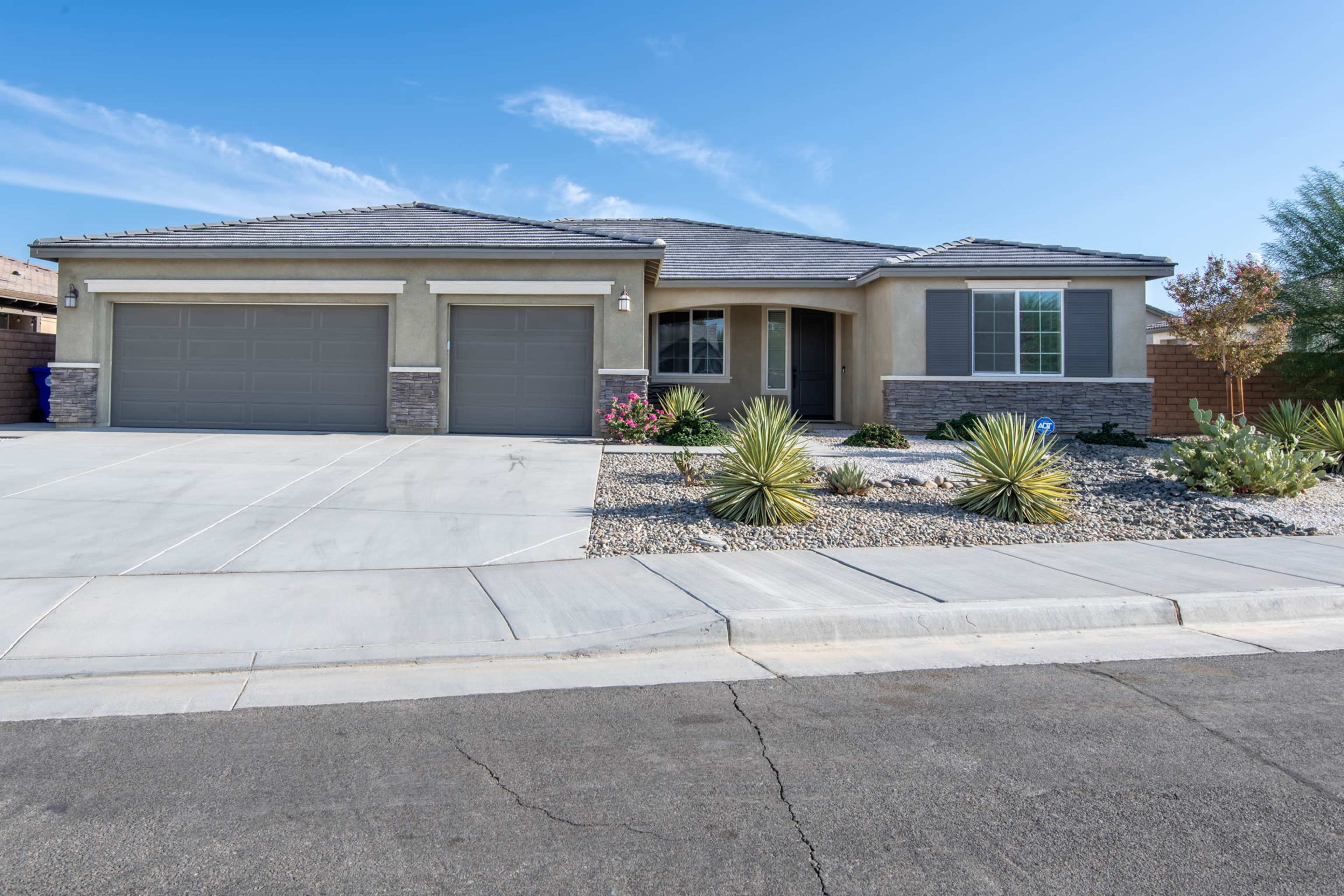 A single-story house with a two-car garage, surrounded by low-maintenance landscaping and a clear blue sky.