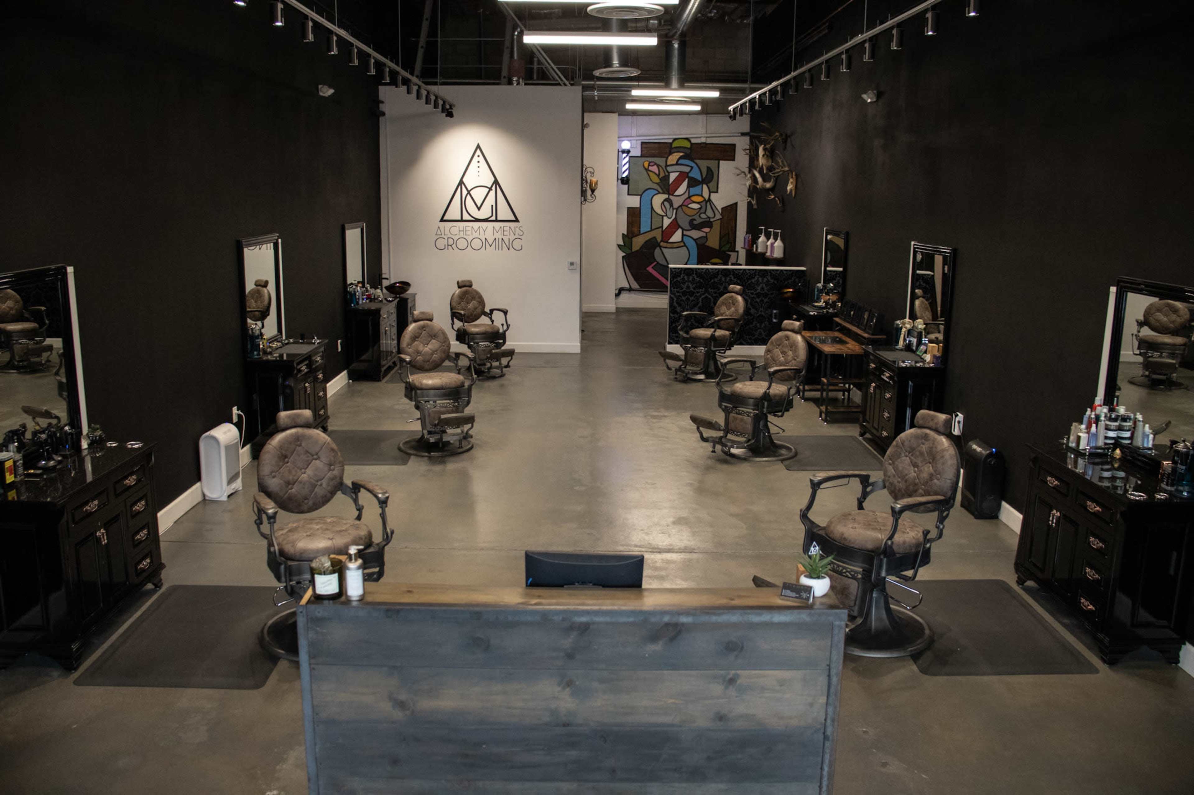 An interior view of a grooming salon featuring multiple styling chairs, large mirrors, and a reception counter, all set against a dark-colored wall.