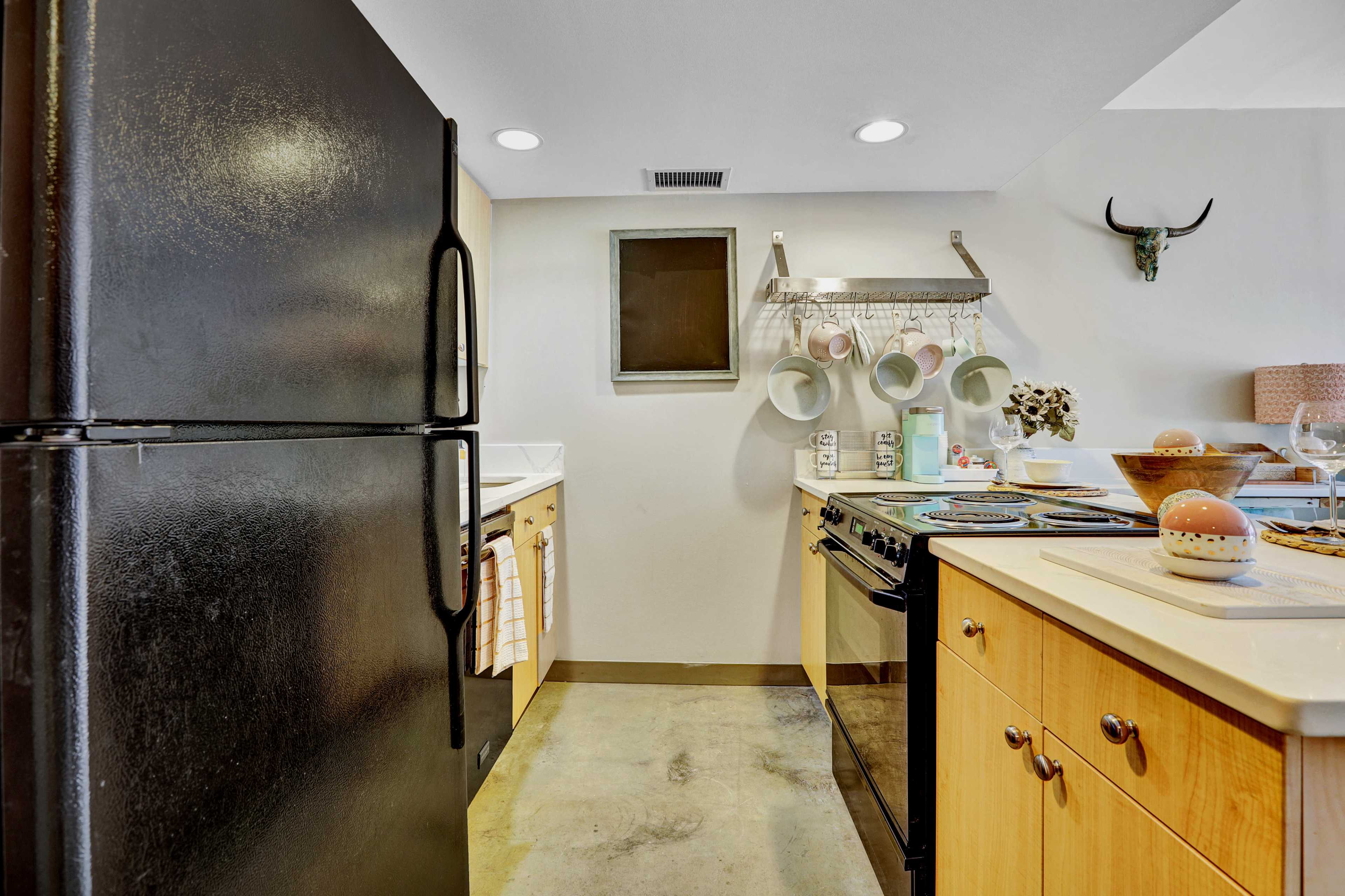 A kitchen featuring a black refrigerator, a white sink, and wooden cabinetry, with cookware and dishware arranged on the countertops.