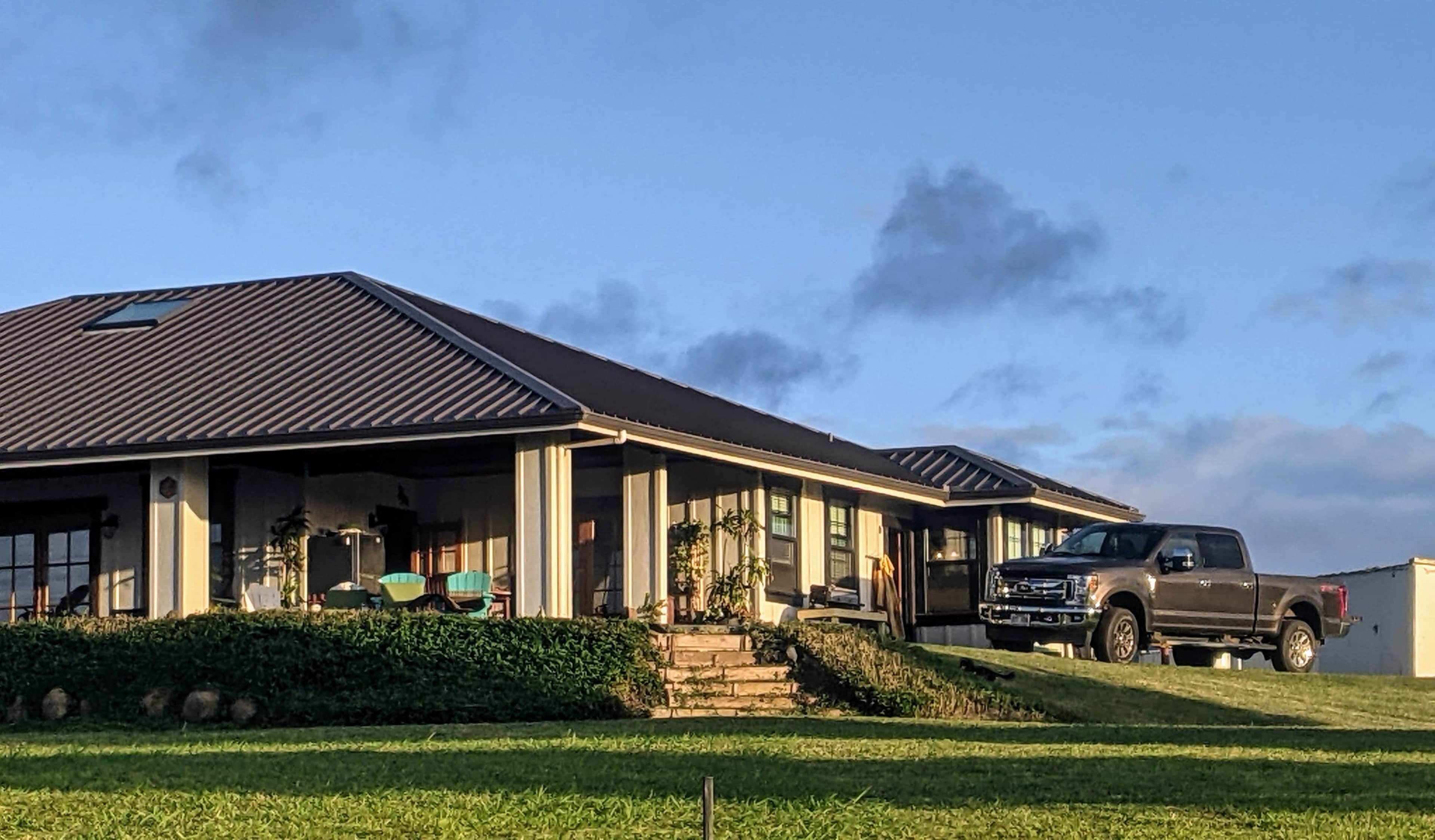 A house with a porch and several steps leads to a grassy area, where a pickup truck is parked on the slope.
