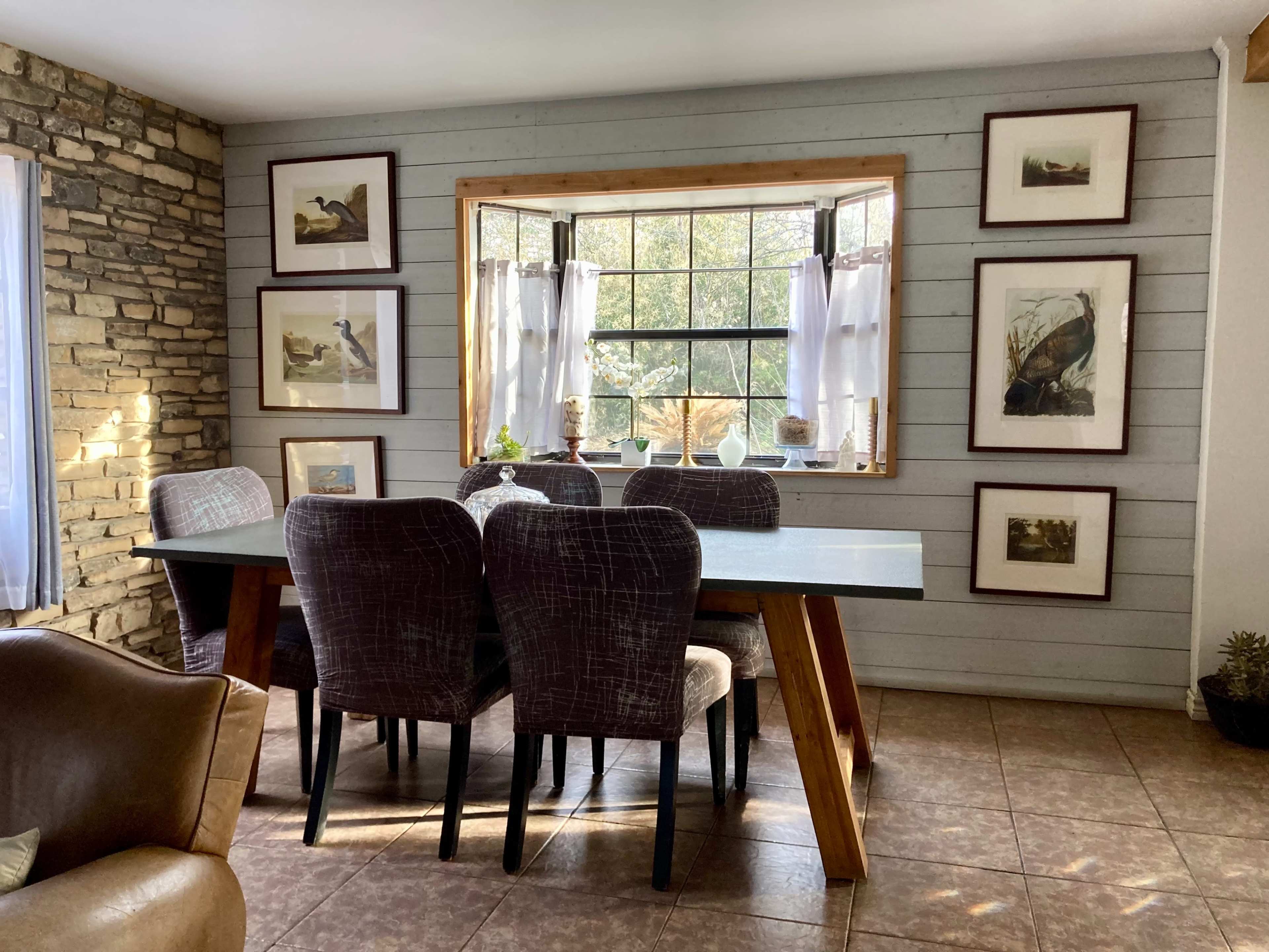 A dining area features a table surrounded by chairs, with framed artwork hanging on the walls and a window allowing natural light to enter.