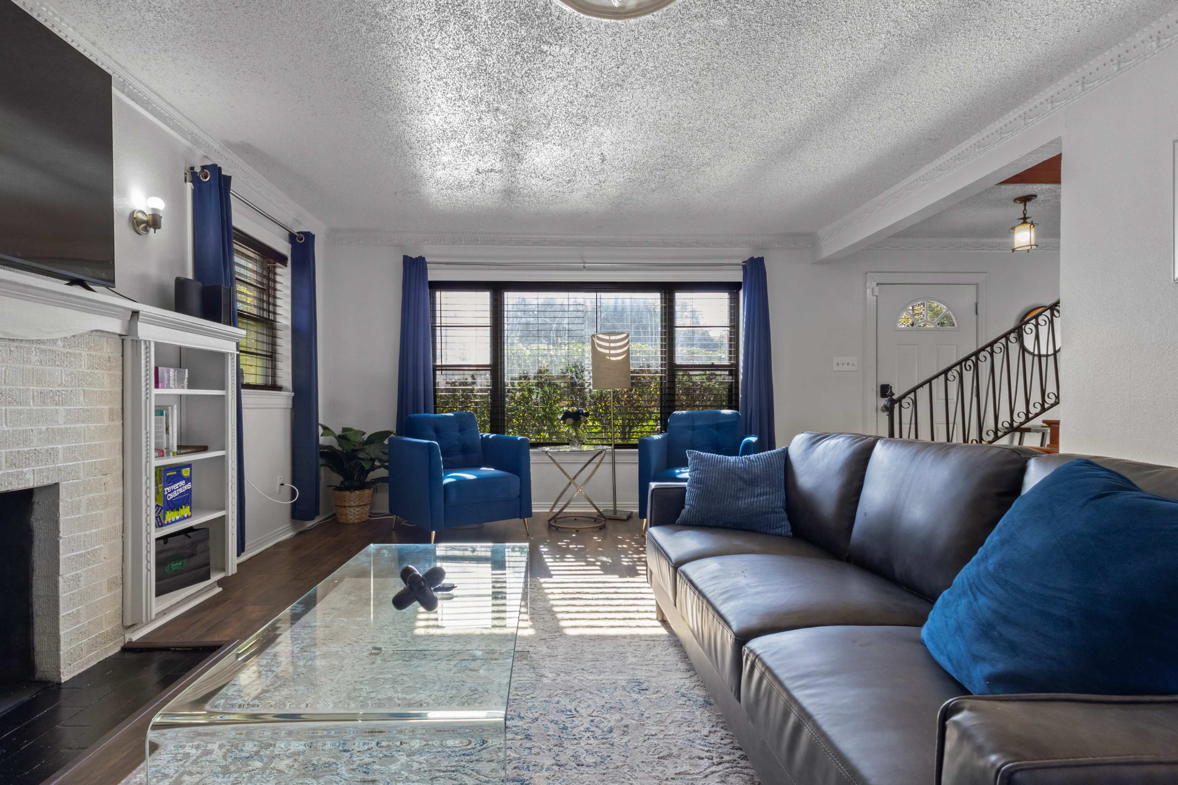 The living room features a blue sofa, a glass coffee table, two armchairs, and a window with blue curtains allowing natural light to enter the space.