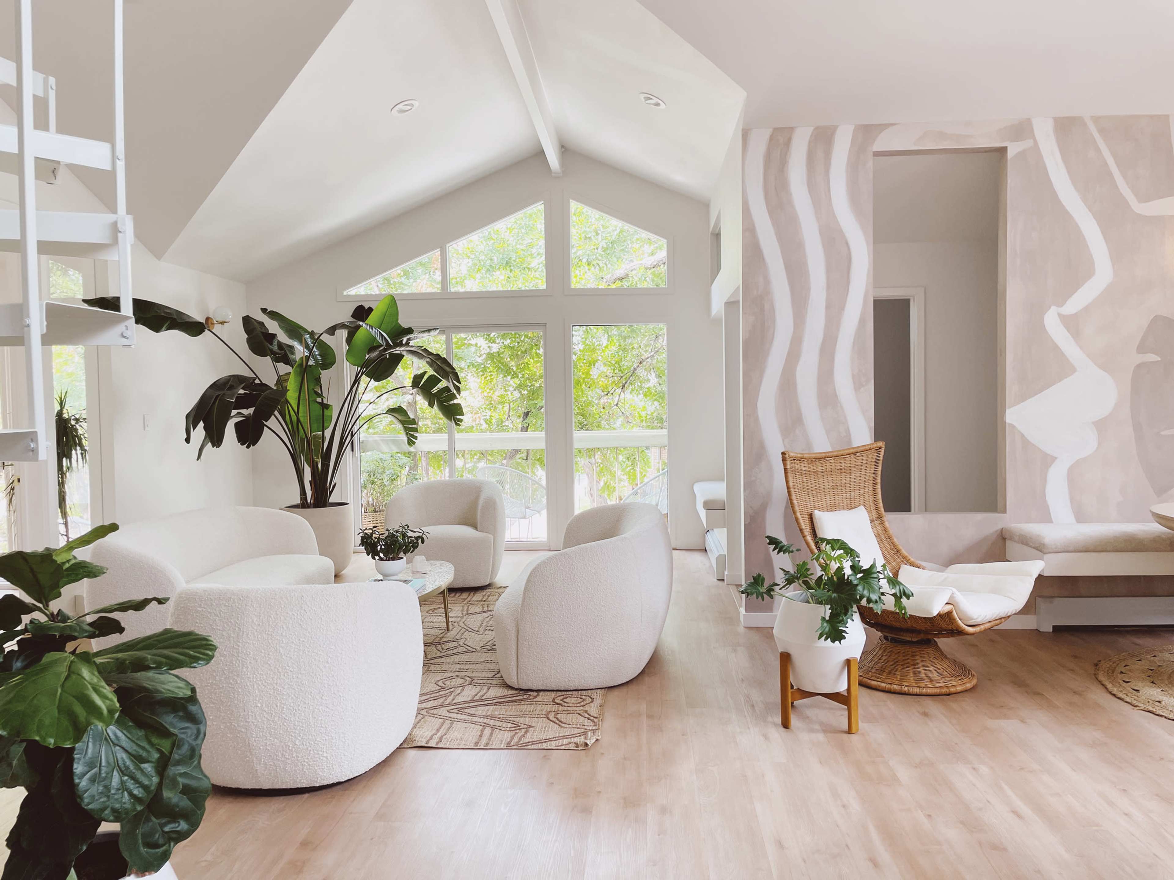 A modern living room with circular white chairs, a woven chair, a large potted plant, and large windows allowing natural light to enter.