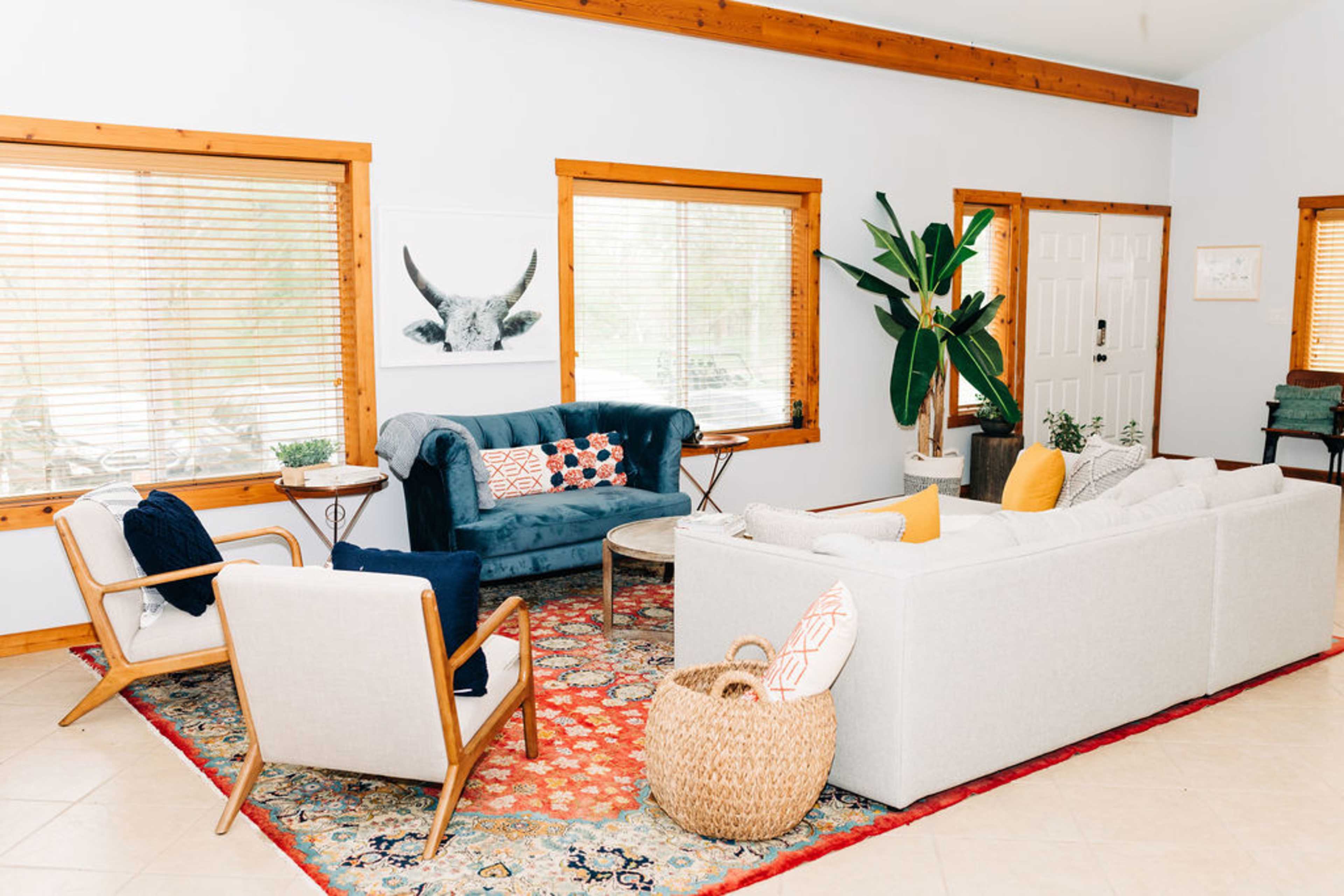 The living room features a sectional sofa, two armchairs, a round coffee table, and a large area rug, with large windows providing natural light.