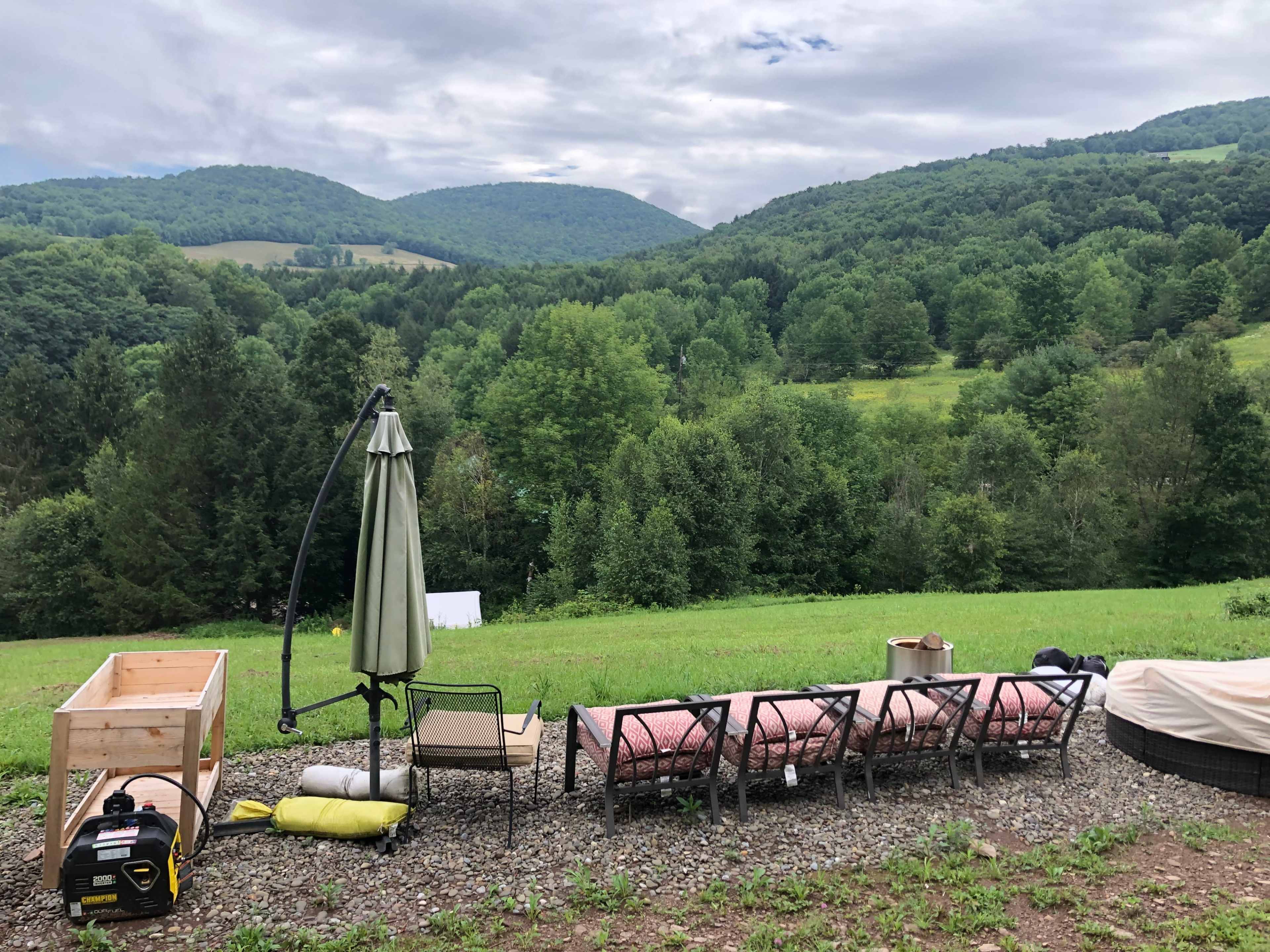 A seating area with lounge chairs and a patio umbrella overlooking a green landscape with rolling hills and trees.