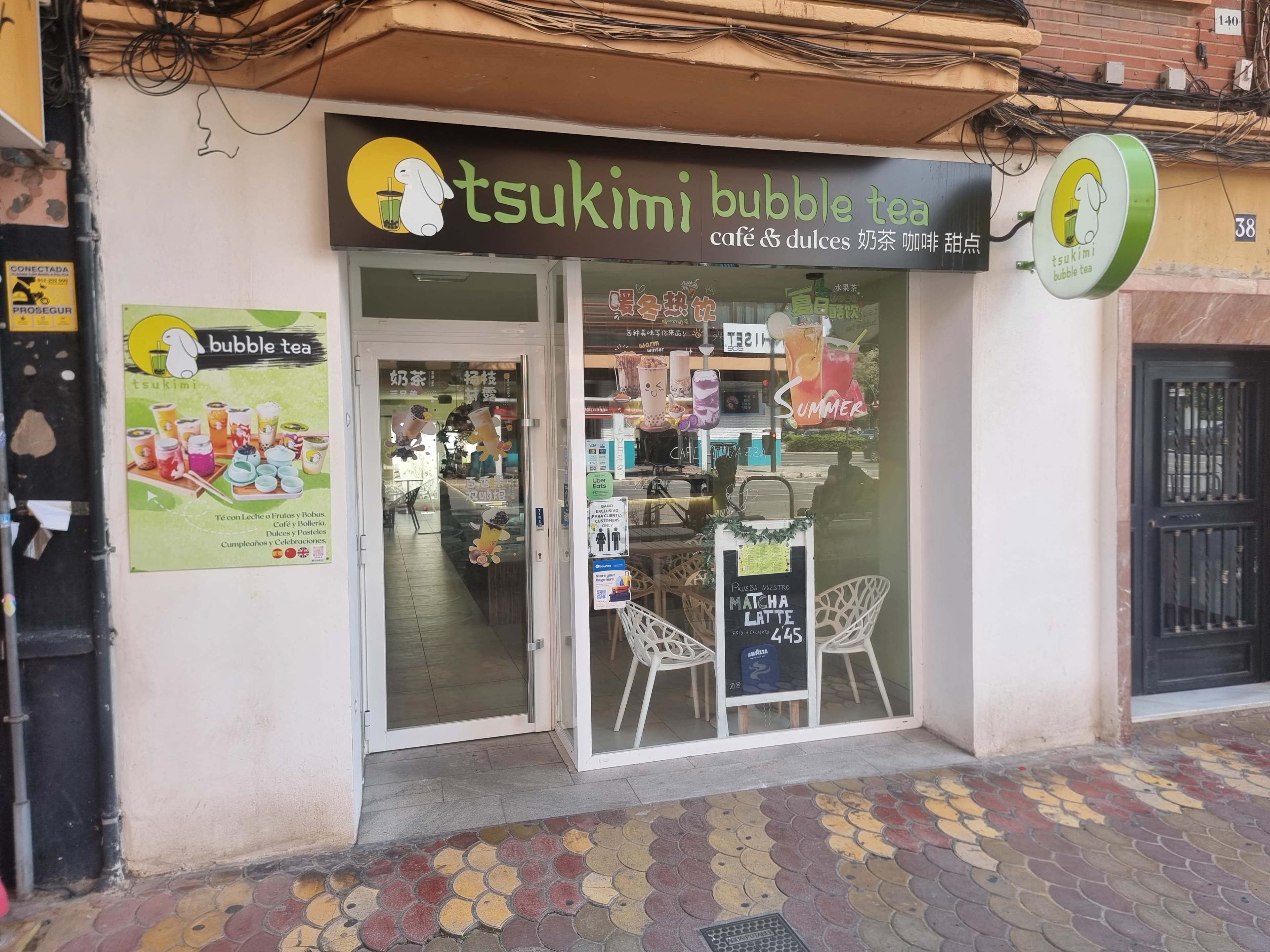 The image shows a storefront of "Tsukimi Bubble Tea," featuring a glass door and a colorful menu displayed outside.