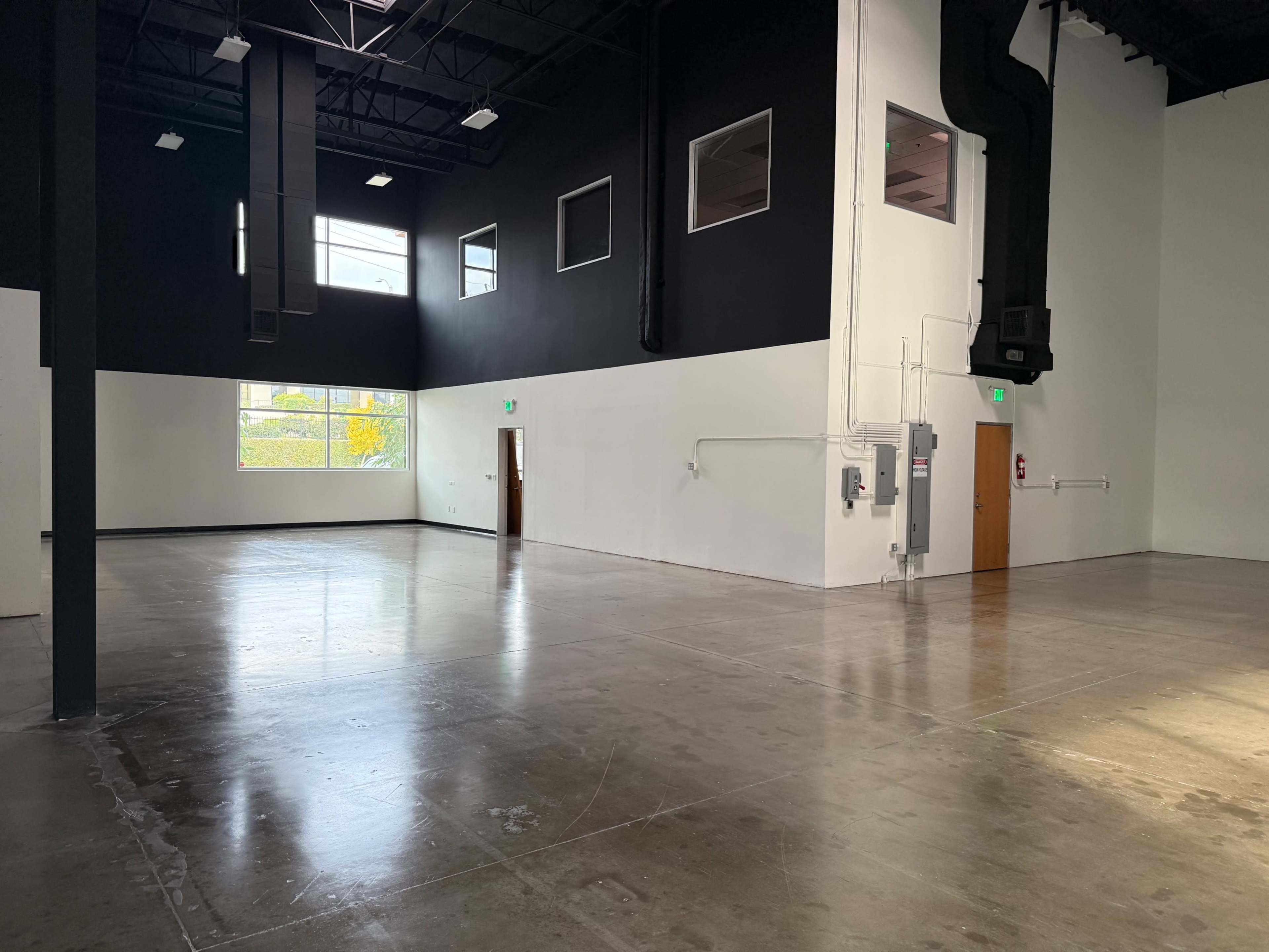 The image shows a spacious, empty interior of a commercial building with concrete floors and large windows.