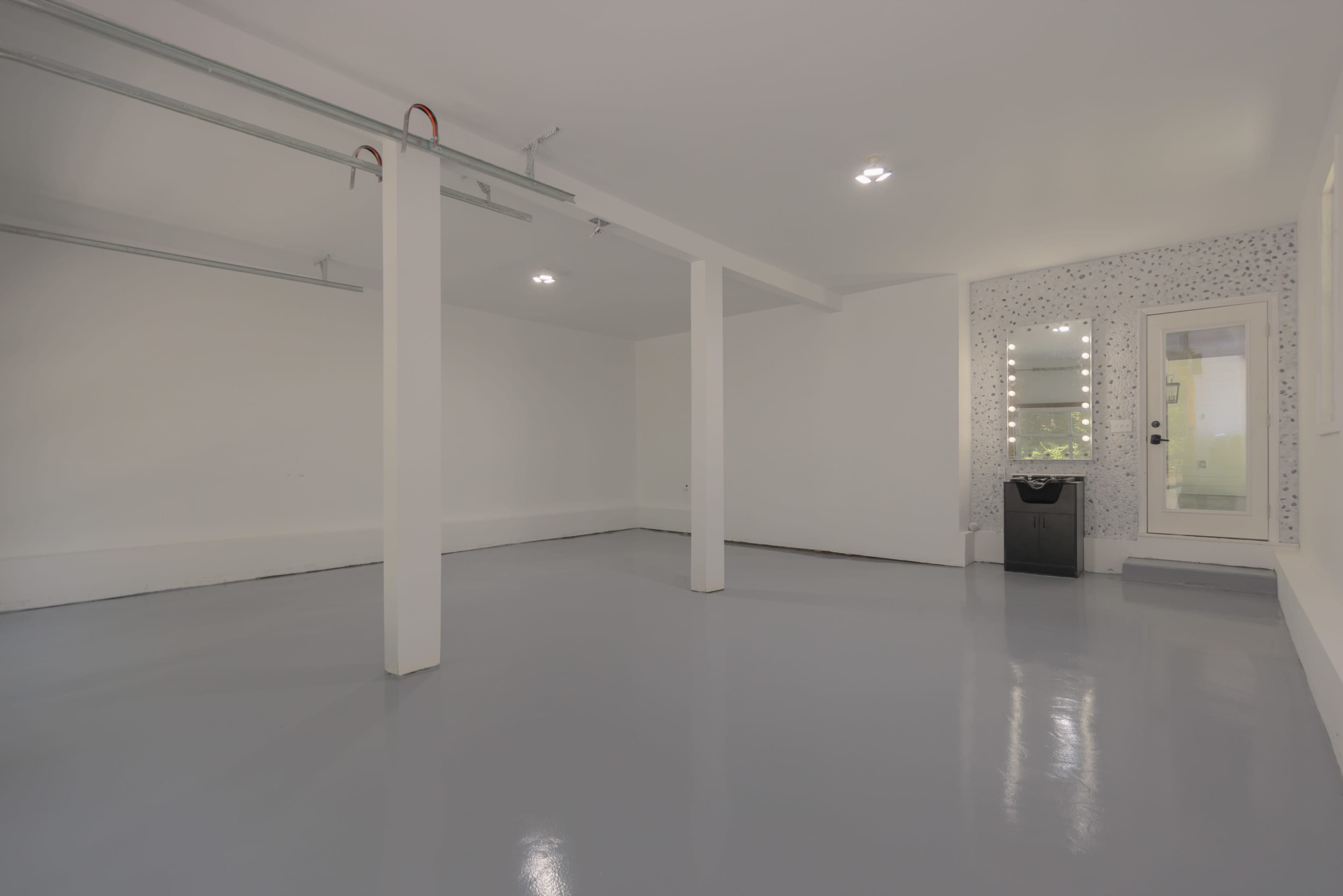 An empty room with gray polished floors, white walls, and a door on one side leading to an exterior area.