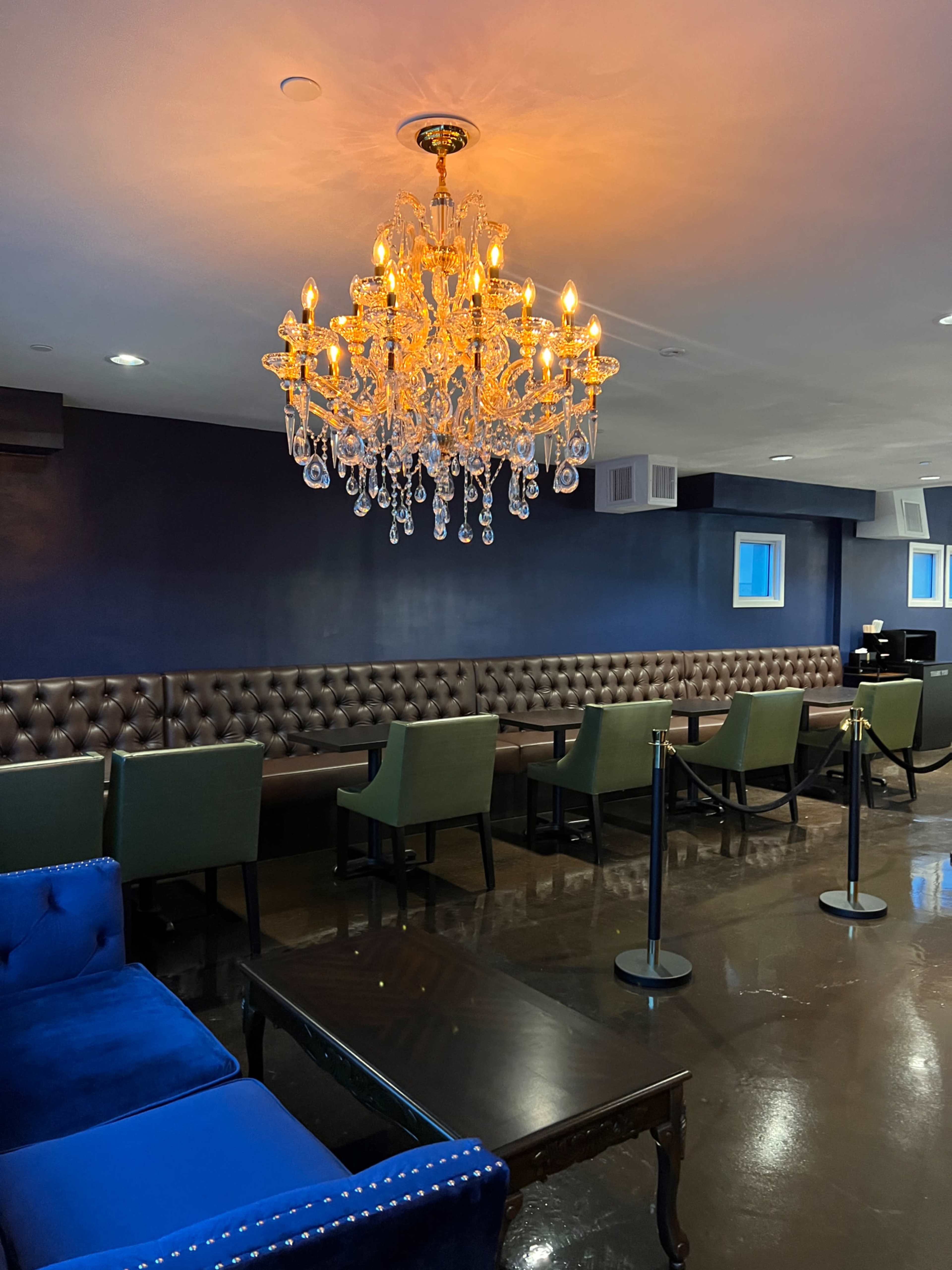 The image shows an elegant waiting area featuring a large chandelier and a combination of dark leather seating and green chairs.