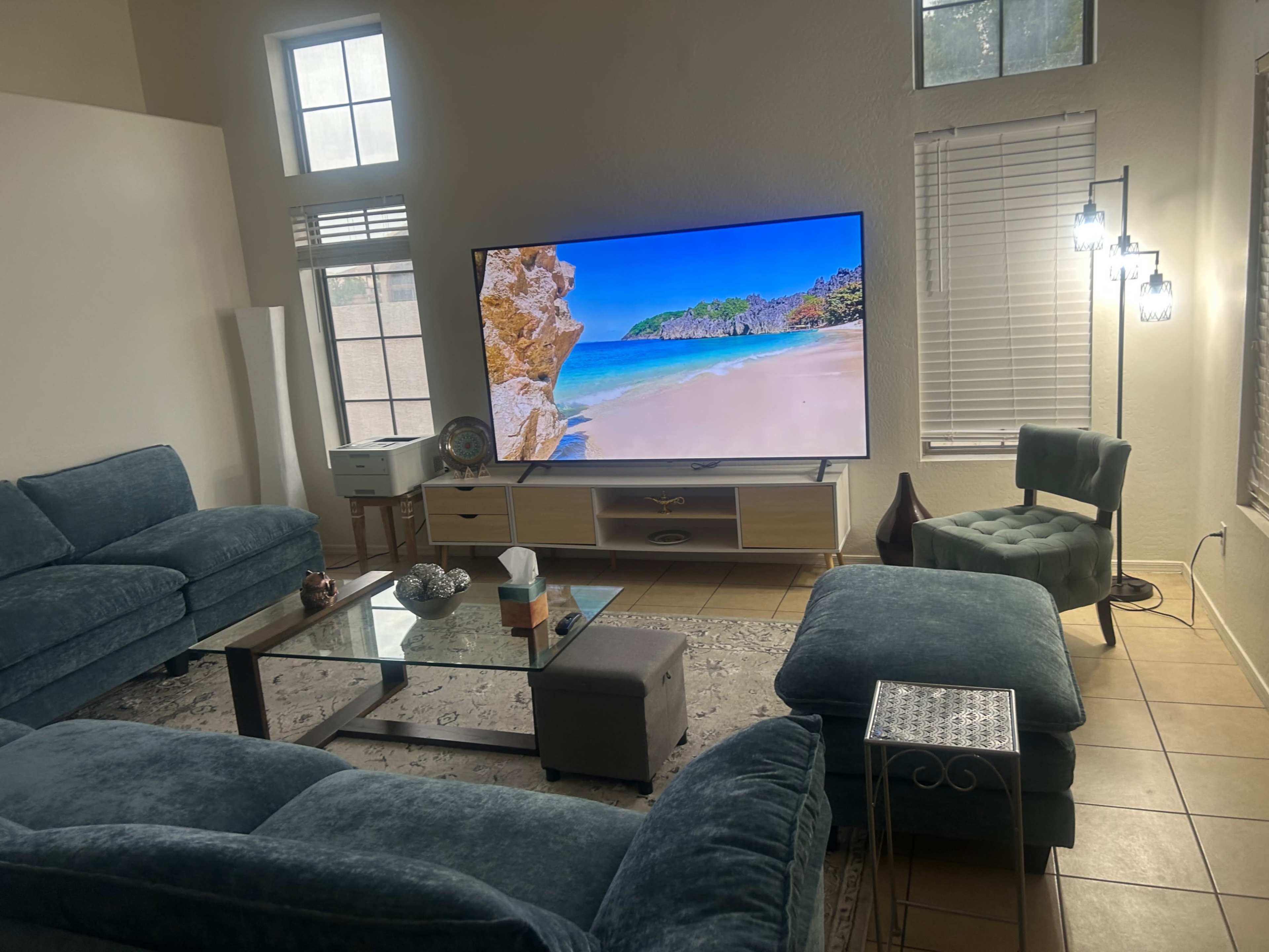 The image shows a living room with a large TV displaying a beach scene, surrounded by a blue sofa set, a glass coffee table, and various decorative items.