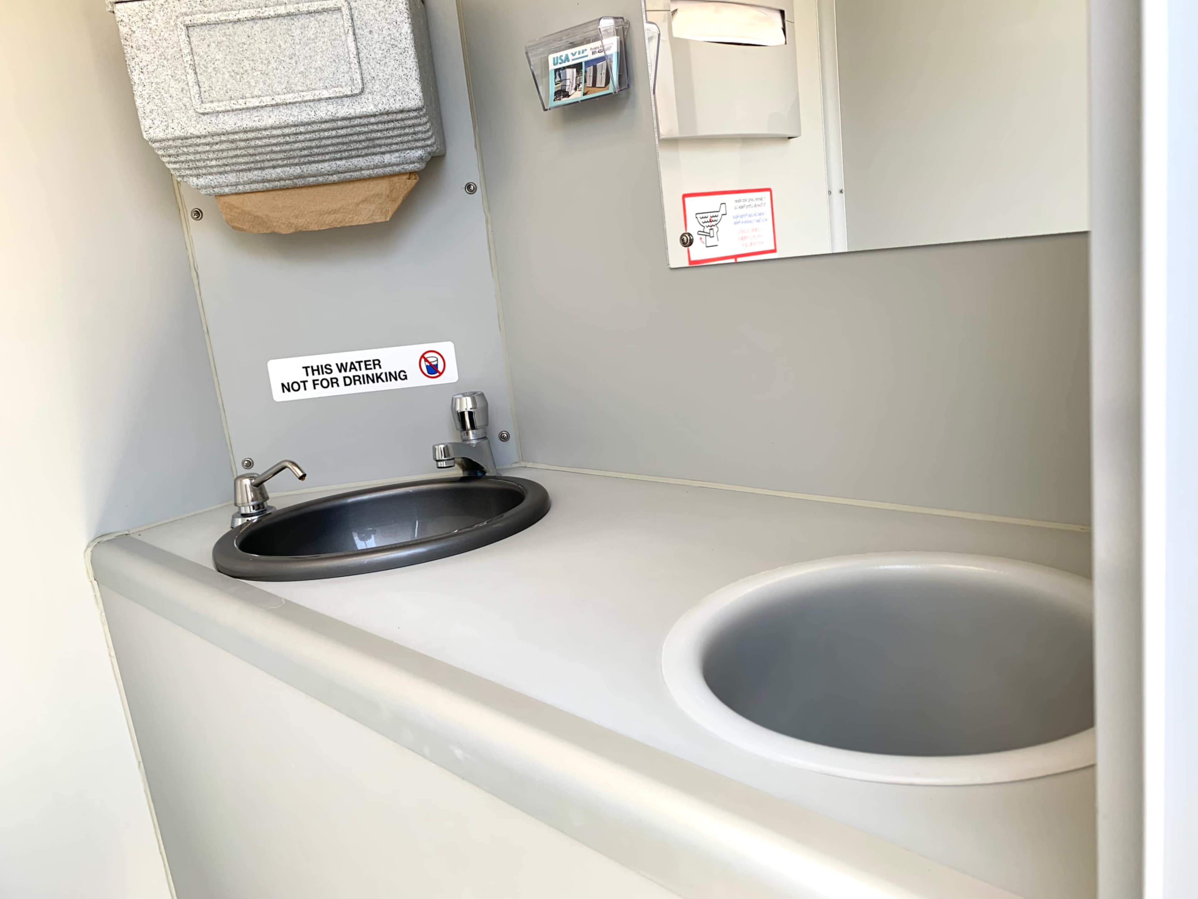The image shows a small sink area with two basins, a hand towel dispenser, and a mirror in a compact space.