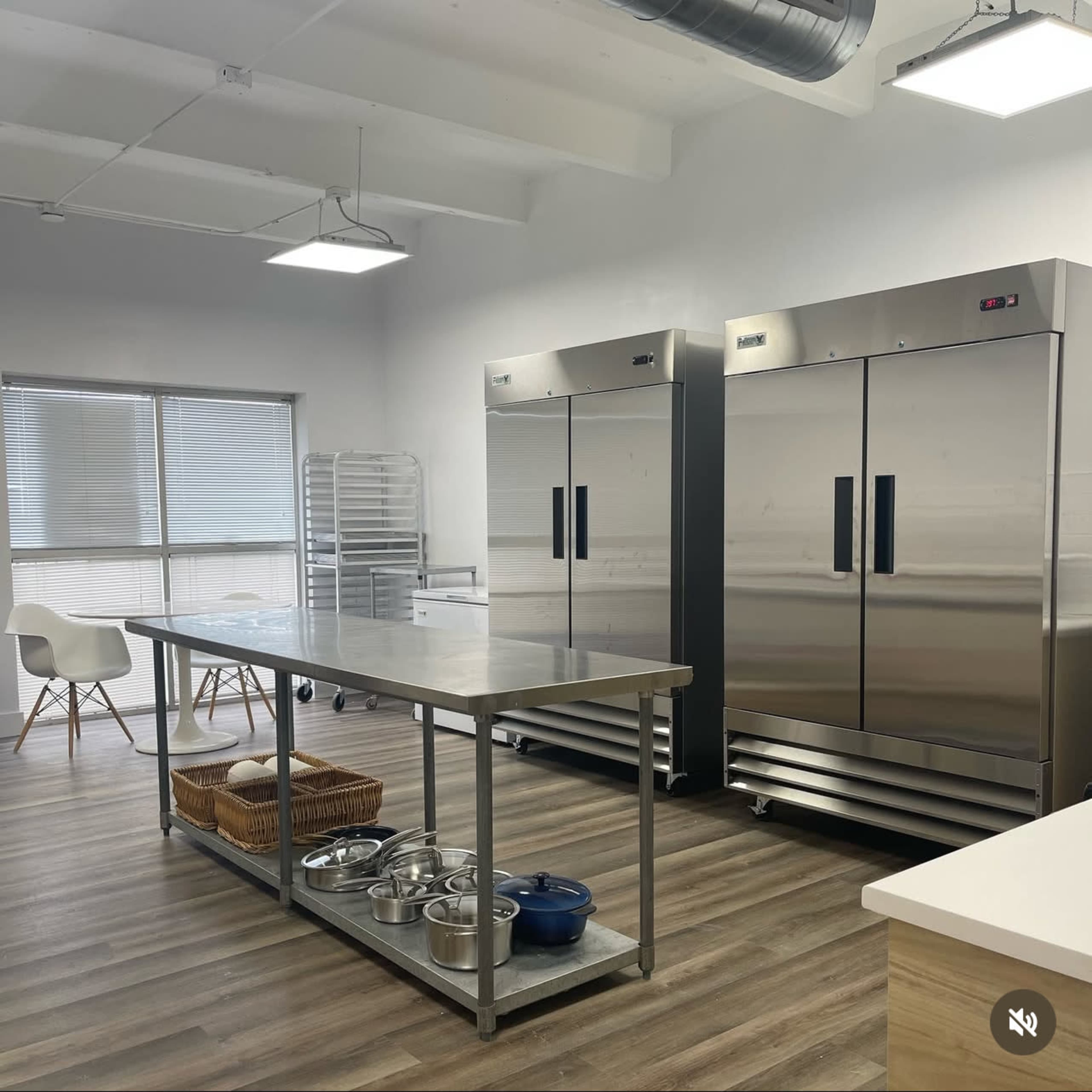The image shows a clean commercial kitchen with two large stainless steel refrigerators, a central prep table, and various kitchen equipment.