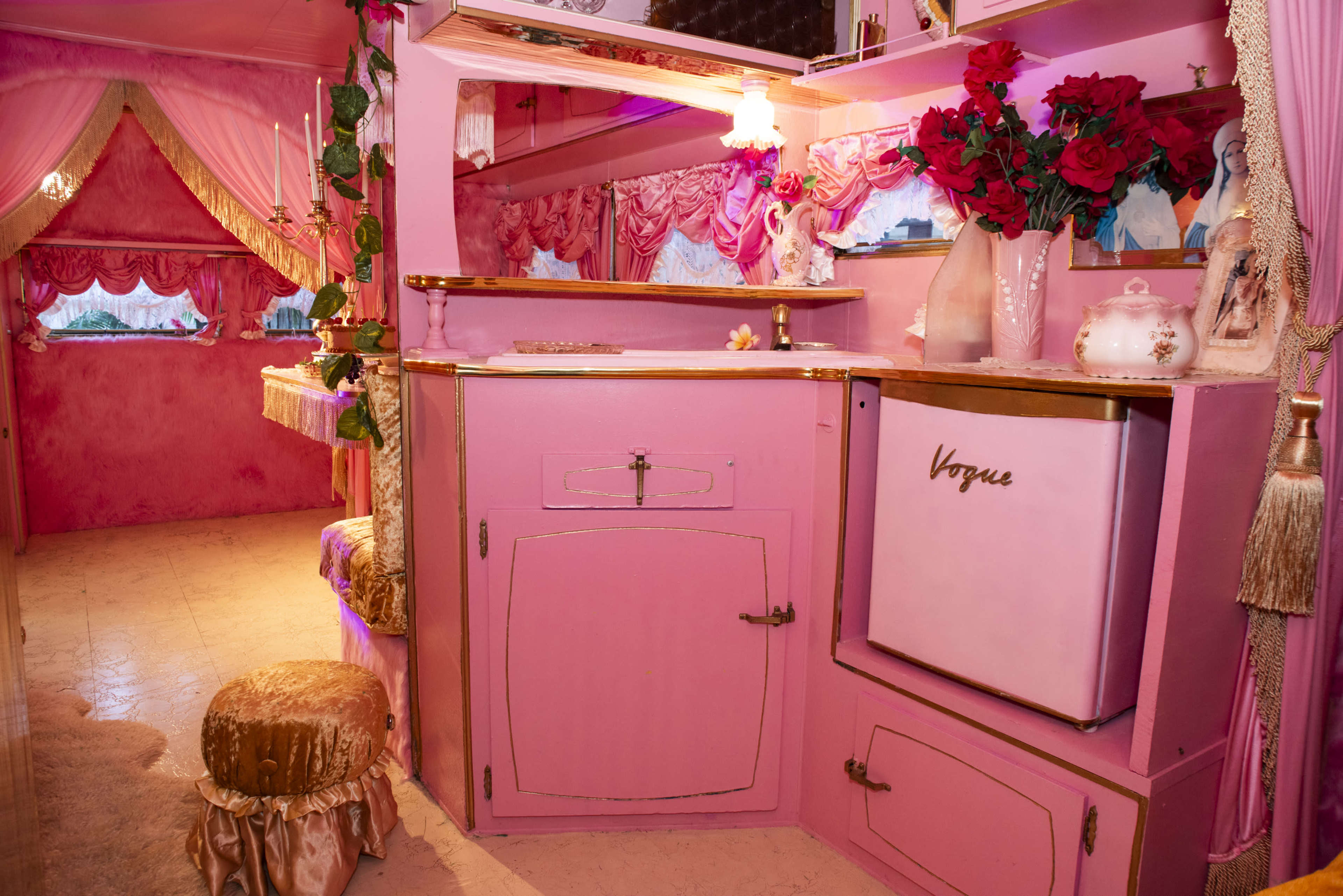 The image depicts a brightly colored room with pink walls, floral decorations, and a small white refrigerator labeled "Vogue."