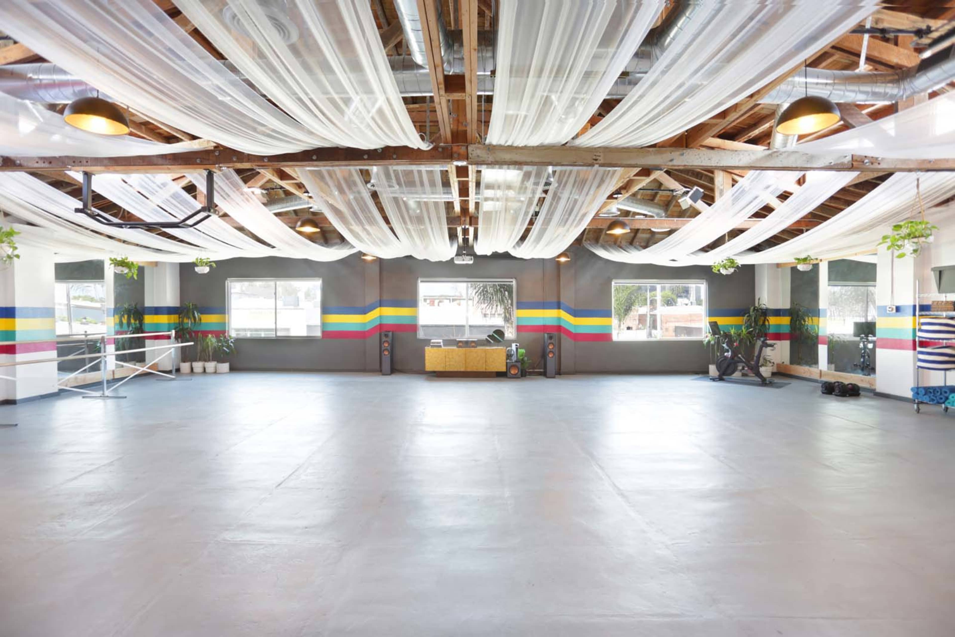 The image shows a spacious indoor venue with a polished concrete floor, draped fabric ceiling, and colorful stripes painted on the walls.