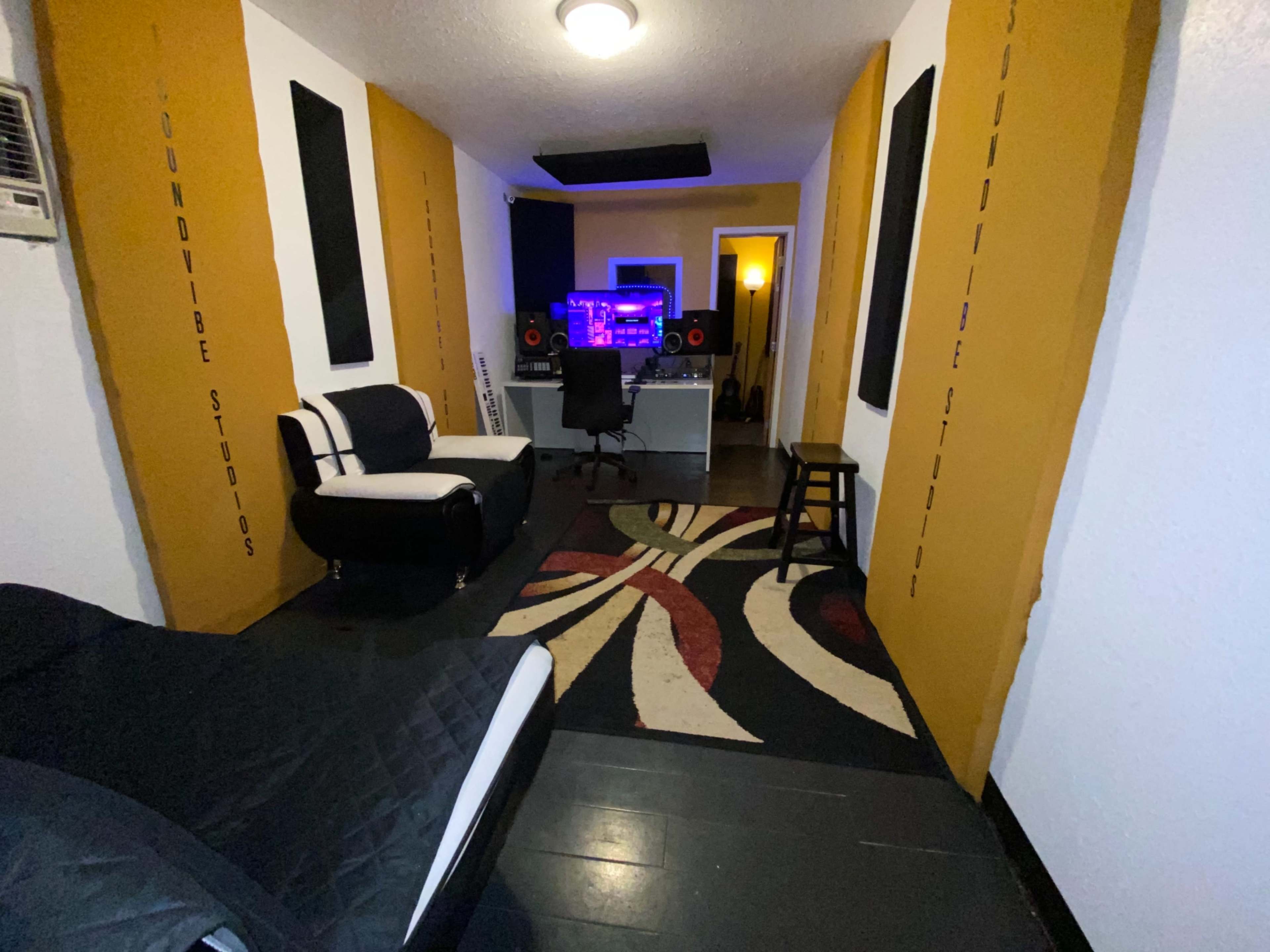 A sound studio with acoustic panels on the walls, a desk equipped with audio equipment, a chair, and a patterned rug.