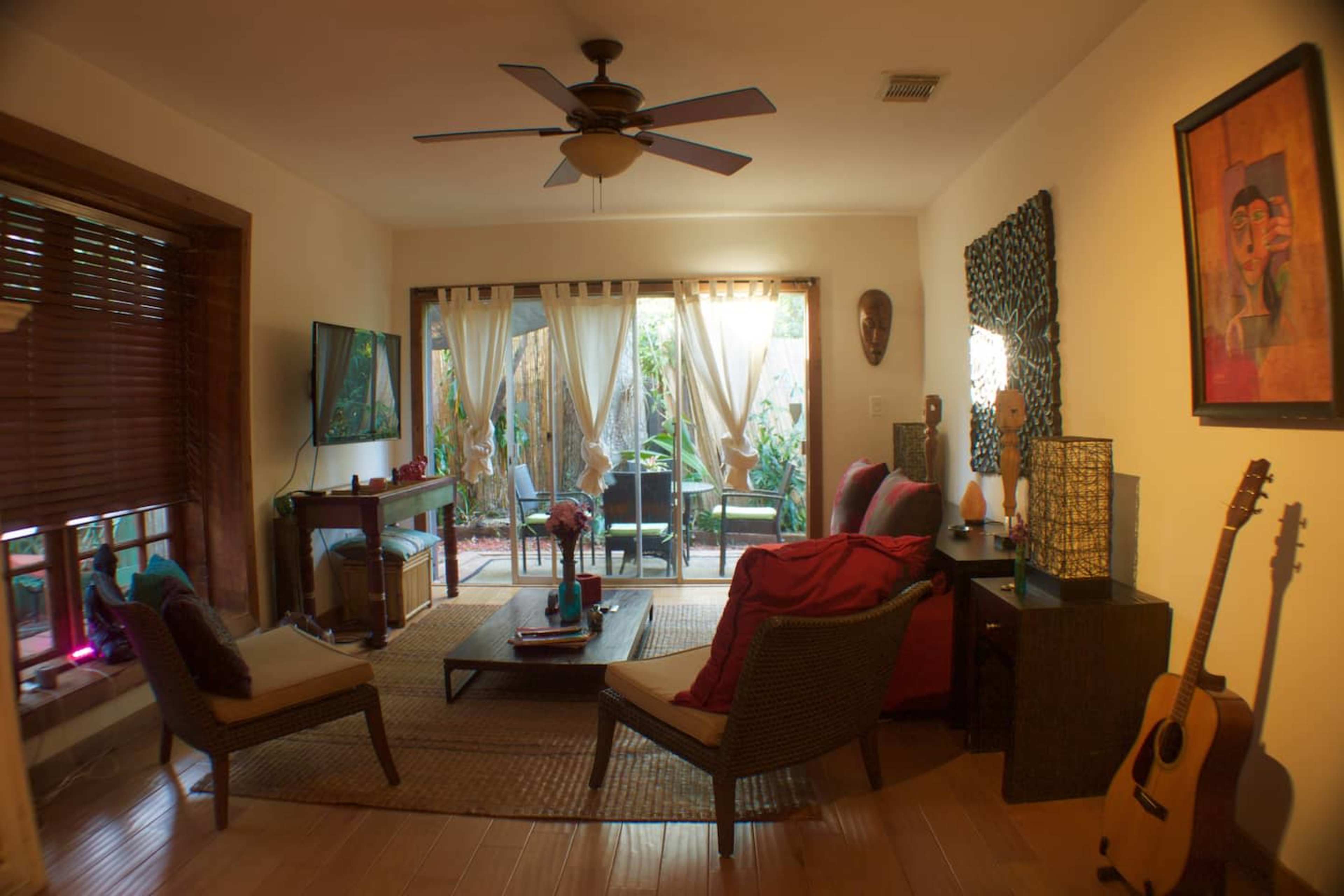 A cozy living room featuring a seating area with two chairs, a coffee table, and a view of a small garden through sheer curtains.