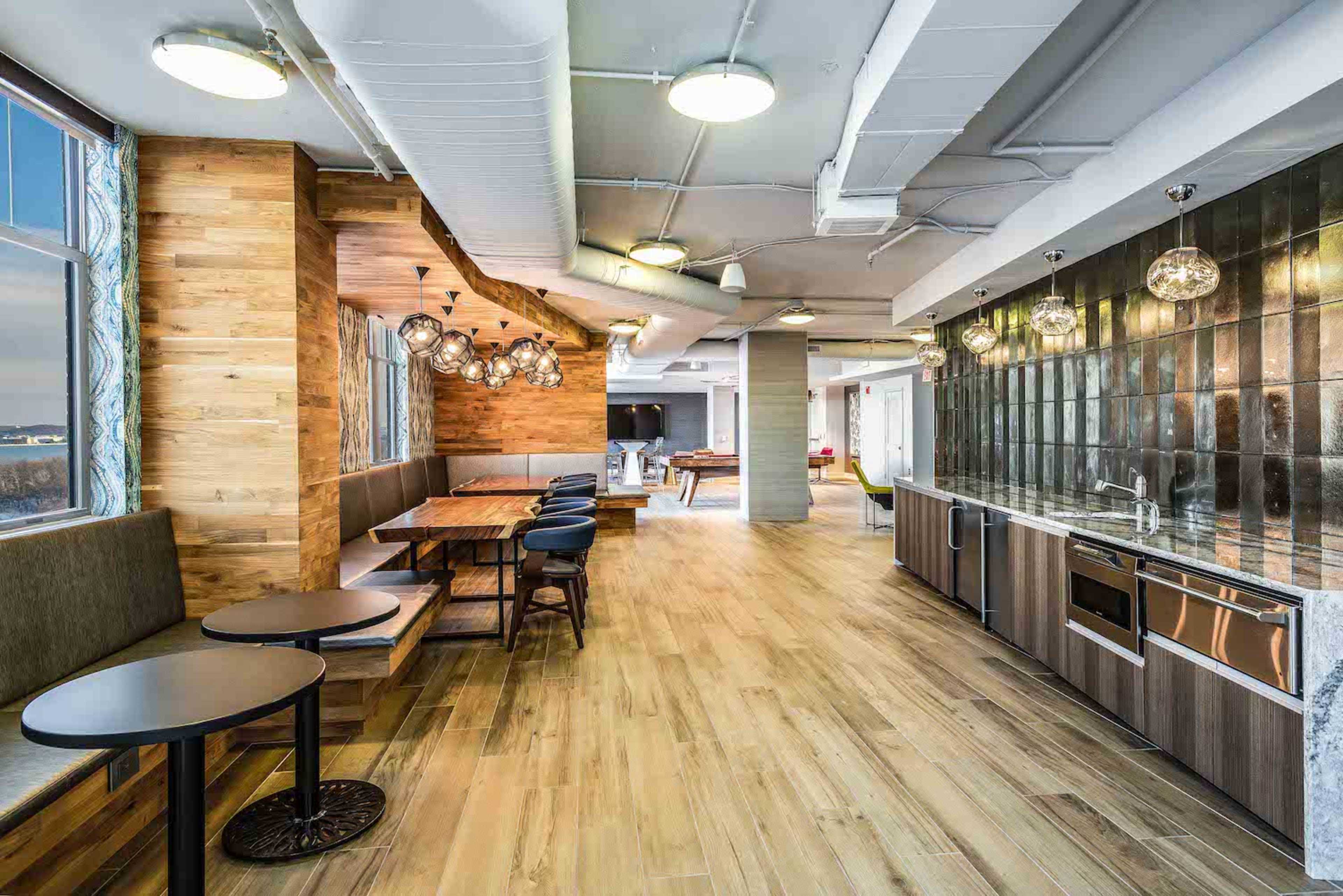 A modern communal kitchen and dining area with wooden accents, sleek surfaces, and both table and seating arrangements.