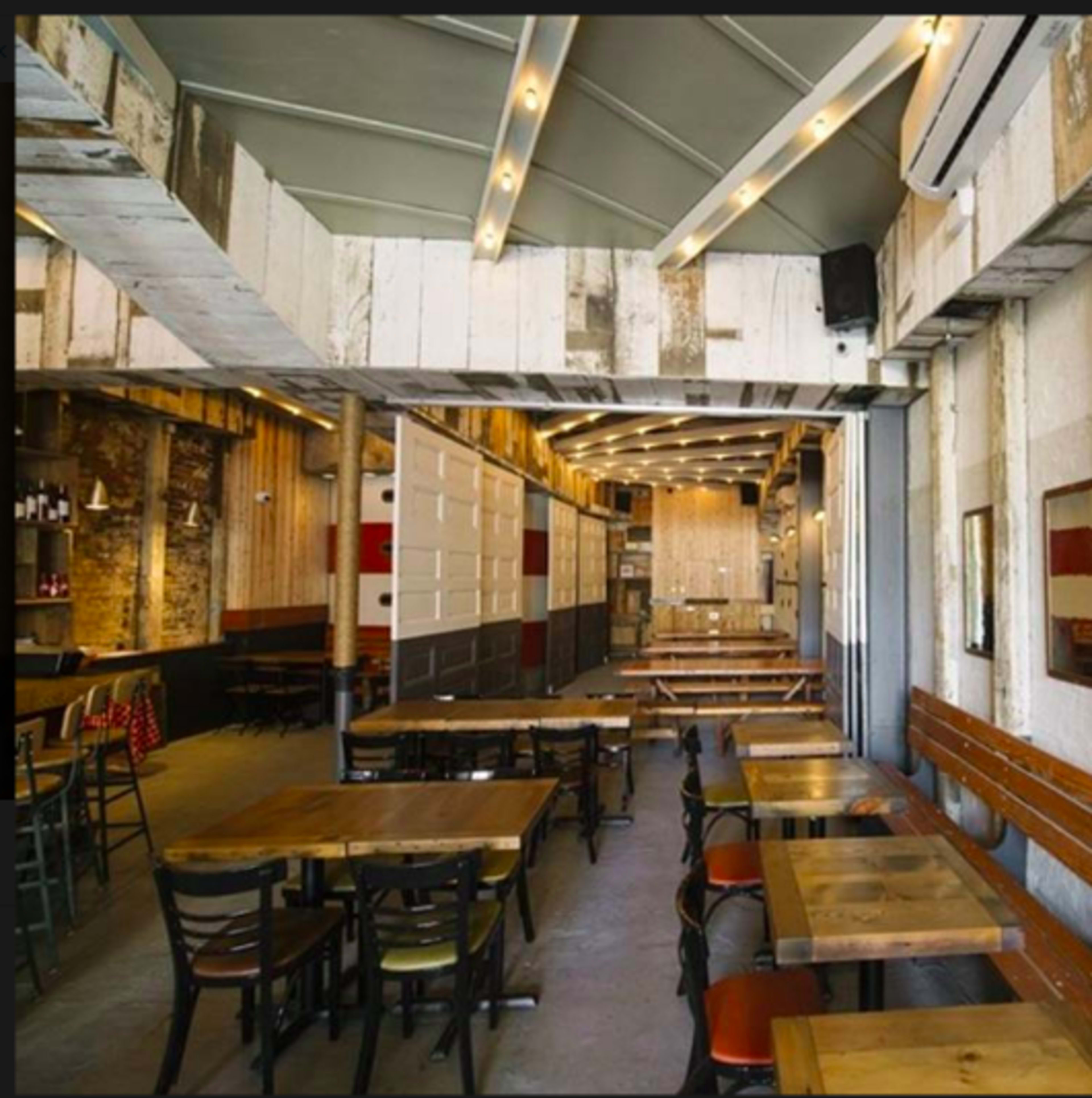 The image shows an empty restaurant interior with rustic wooden walls, multiple tables, and benches arranged in a spacious layout.