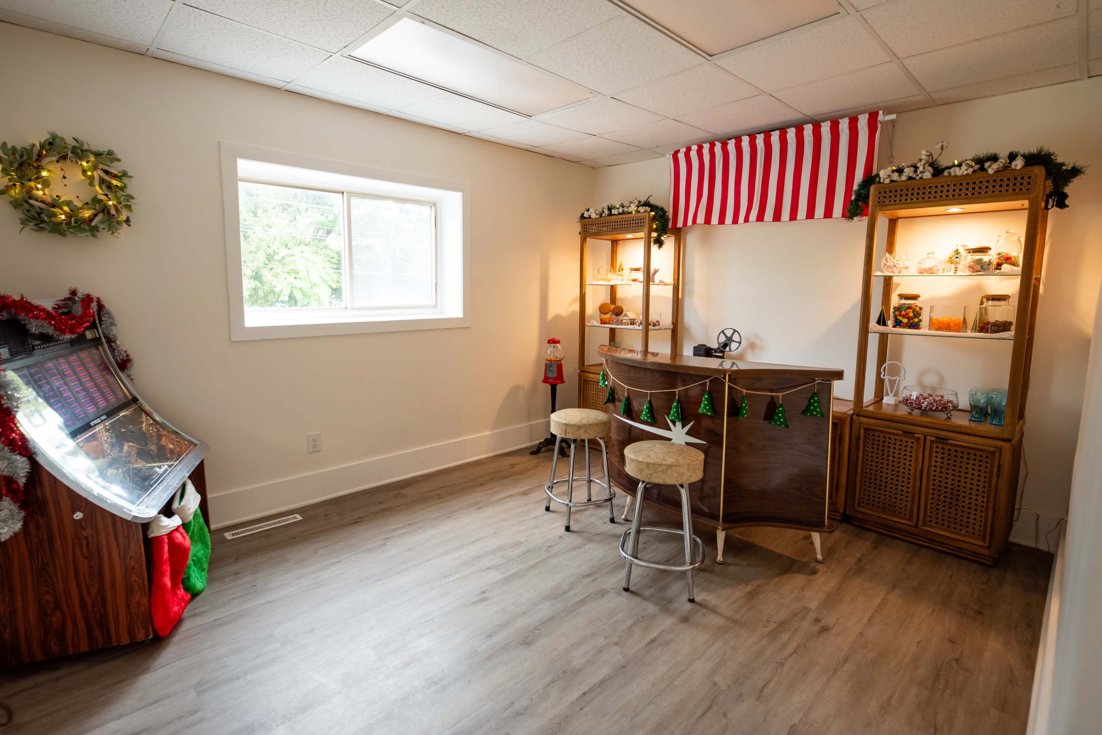 The image shows a small room with a bar counter, shelves filled with jars, and a window, decorated for a festive occasion.