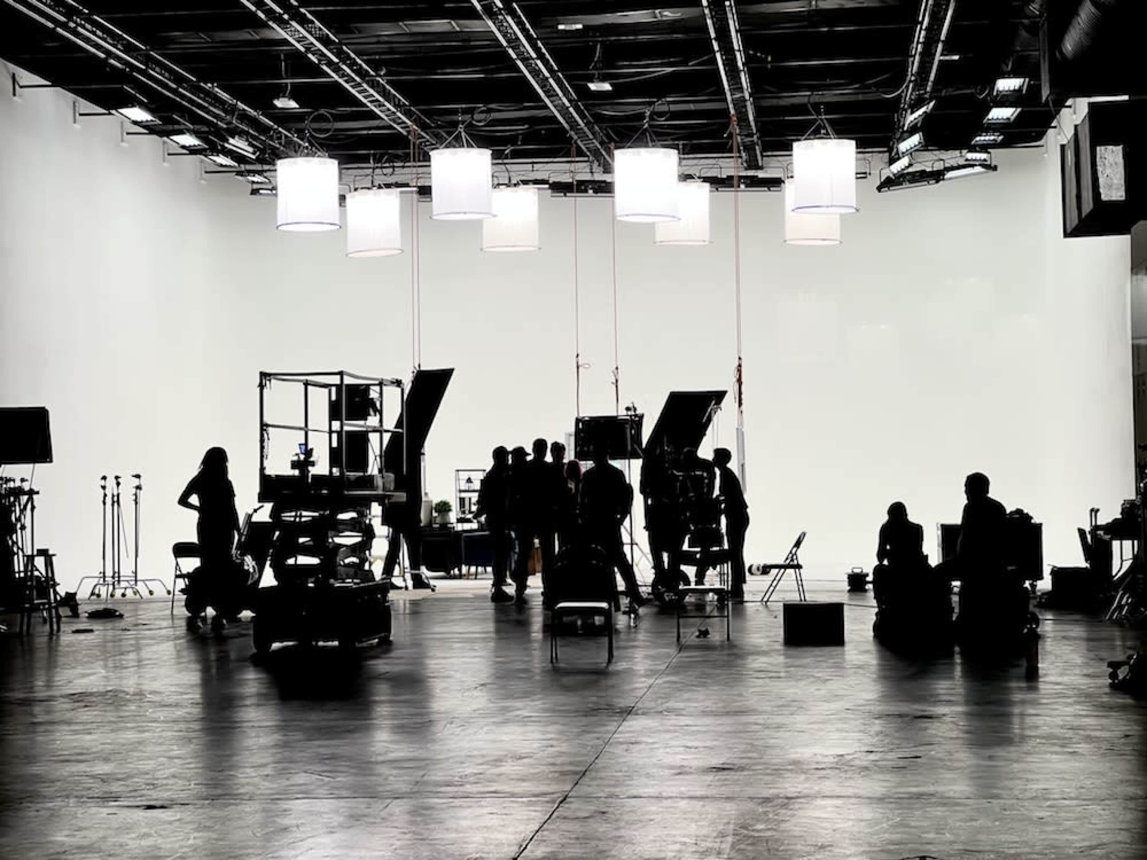A film set is illuminated by overhead lights, featuring various equipment and crew members working in the foreground.