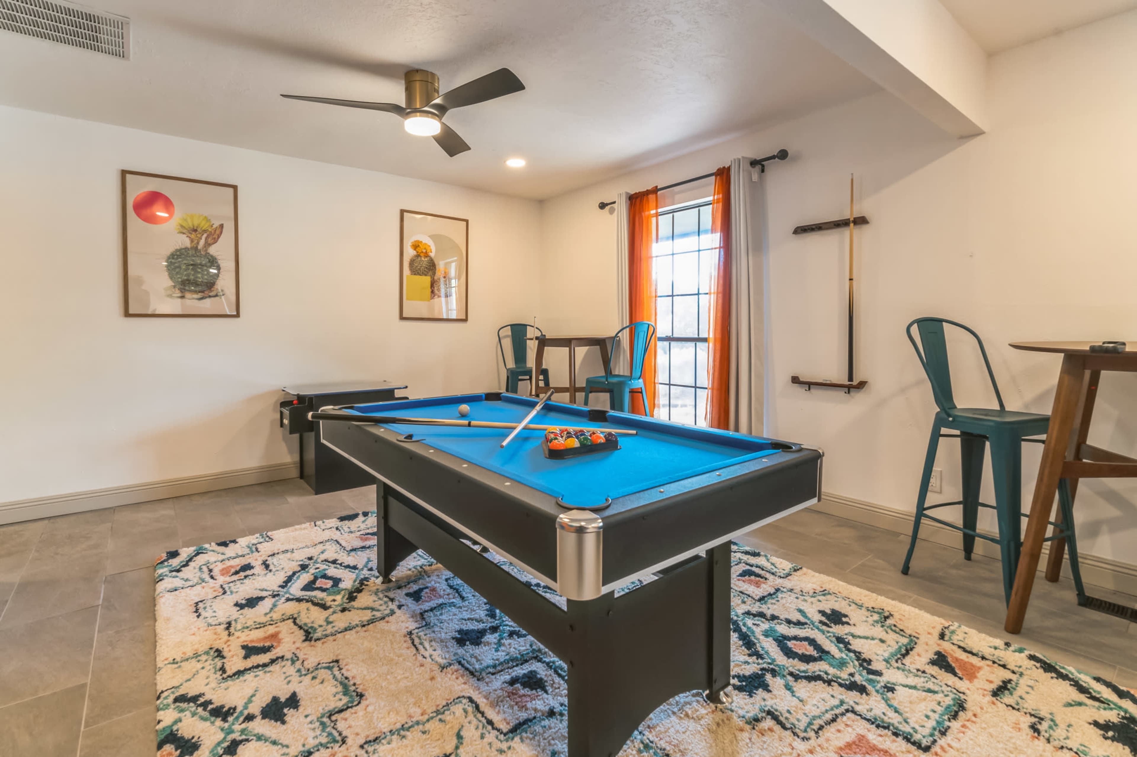 A recreational room featuring a pool table with a blue felt surface, surrounded by seating and decor, including framed artwork on the walls.
